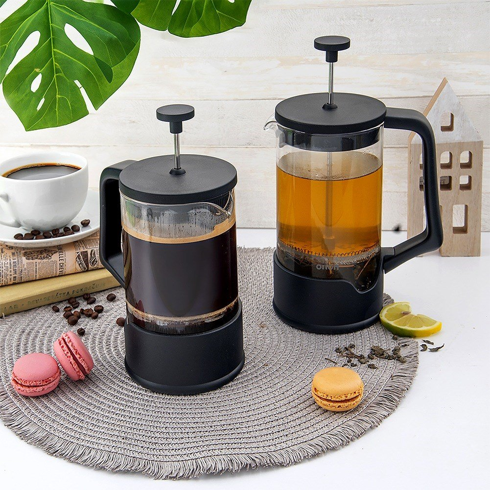 Dos cafeteras de prensa francesa, una con café, otra con té, junto a macarons.
