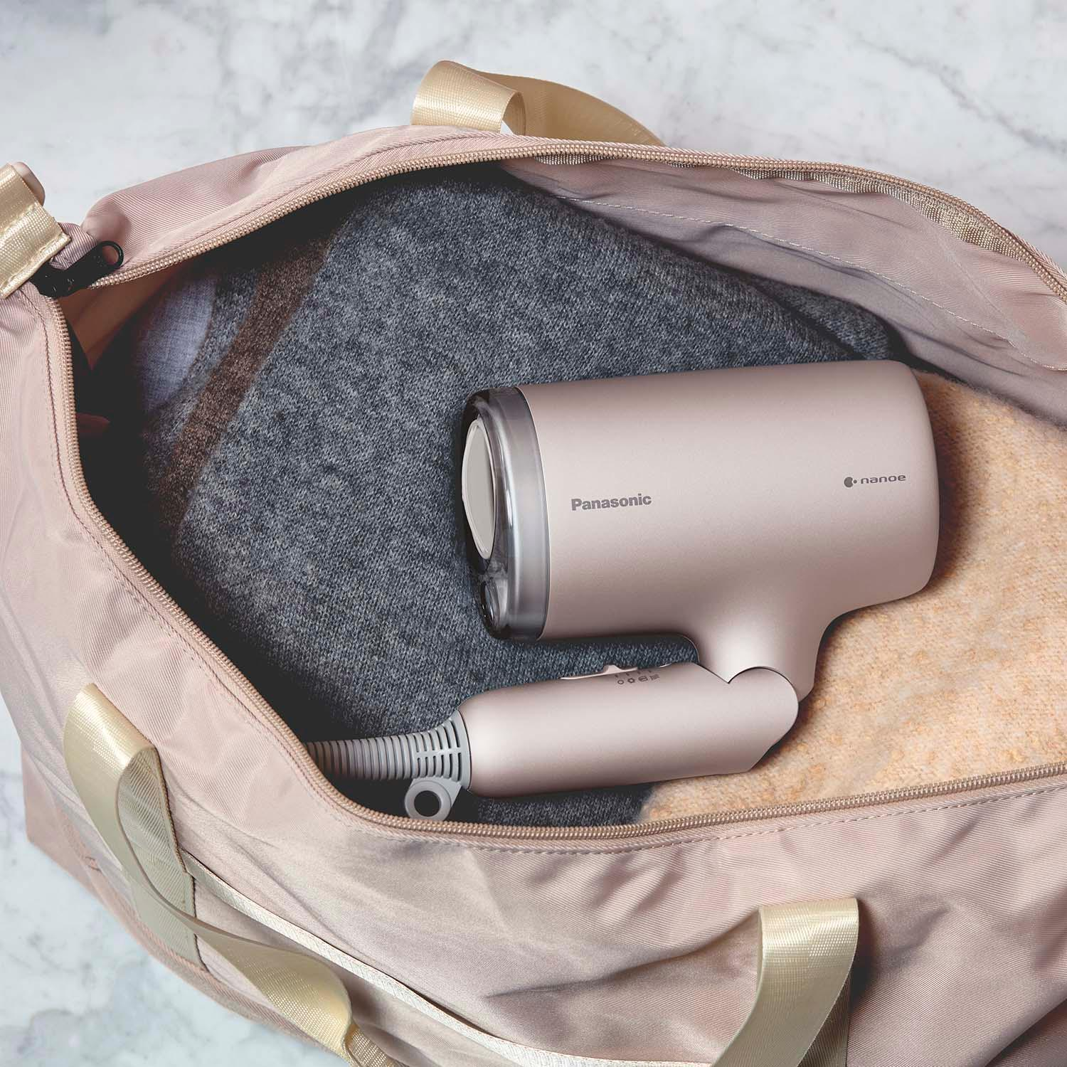 Un asciugacapelli Panasonic oro rosa riposa in una borsa da viaggio rosa sopra i vestiti.