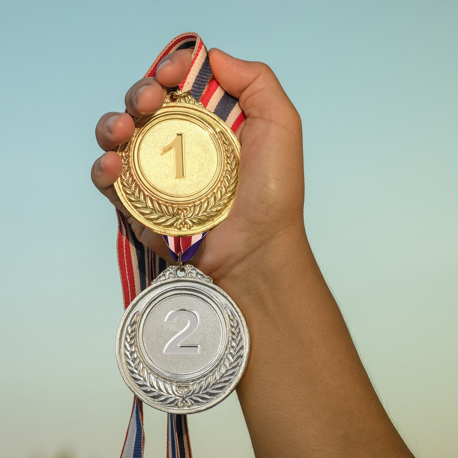 Una mano sostiene una medalla de oro y una de plata con cintas.