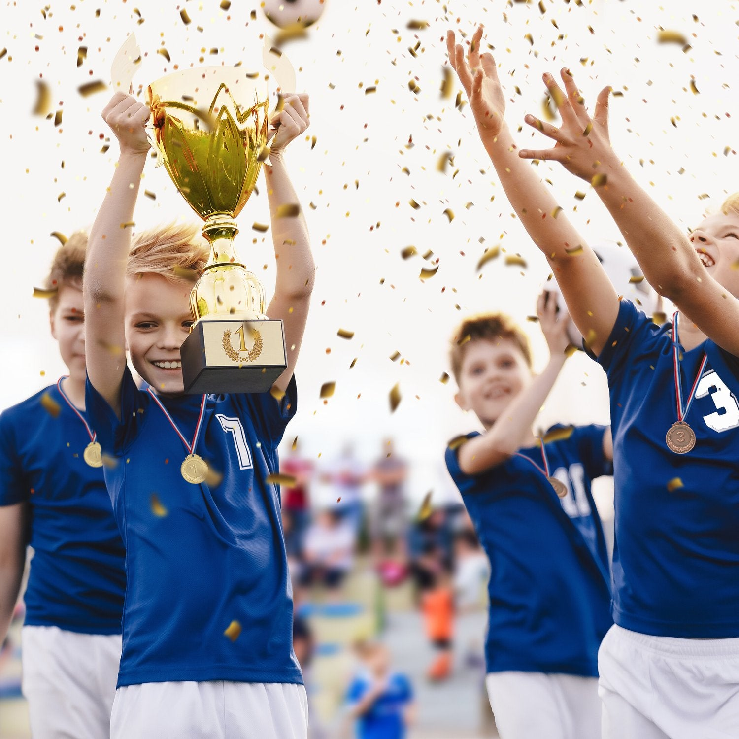 Jóvenes futbolistas en uniforme azul celebran con trofeo y confeti.