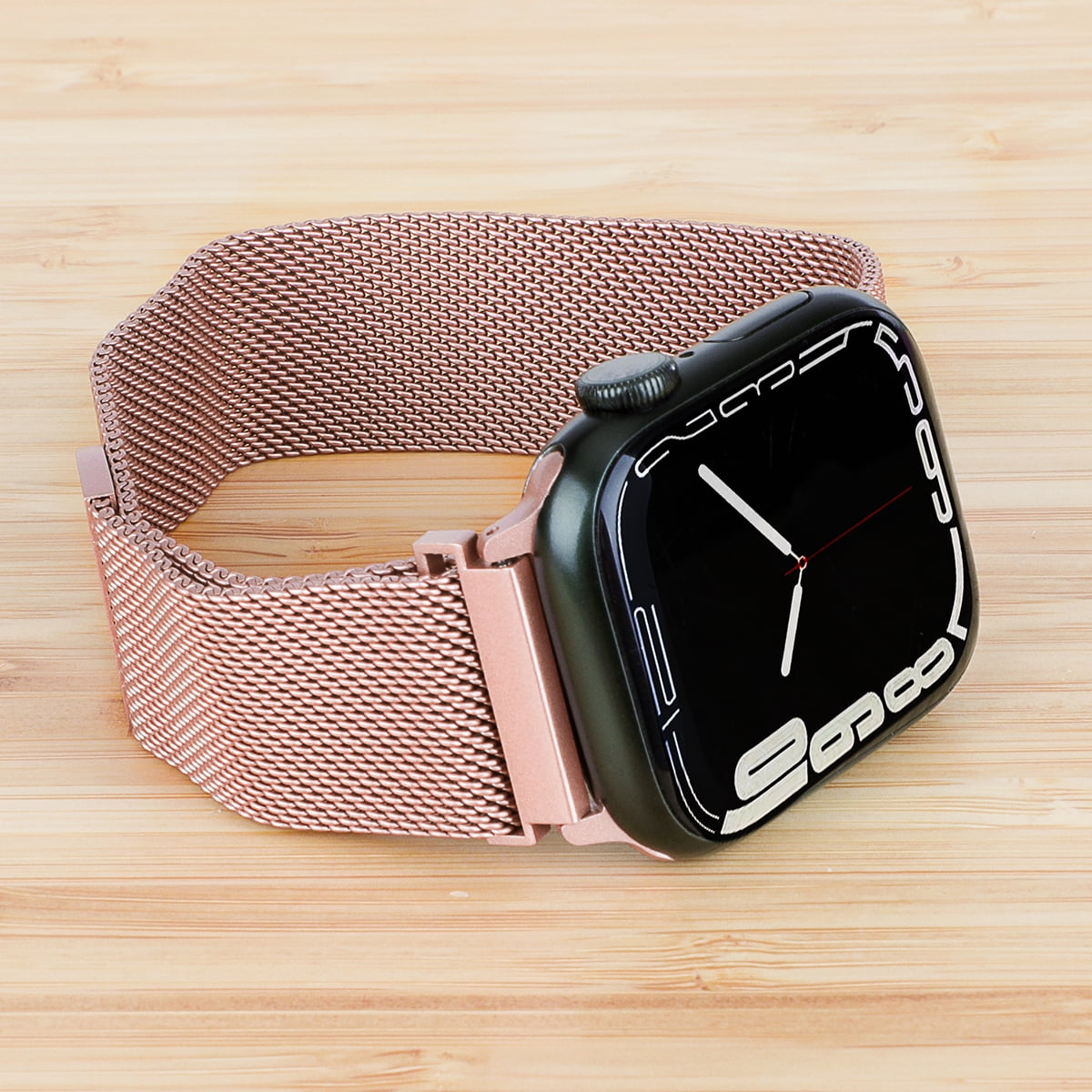 Eine grüne Smartwatch mit roségoldfarbenem Milanaise-Armband auf Holzhintergrund.