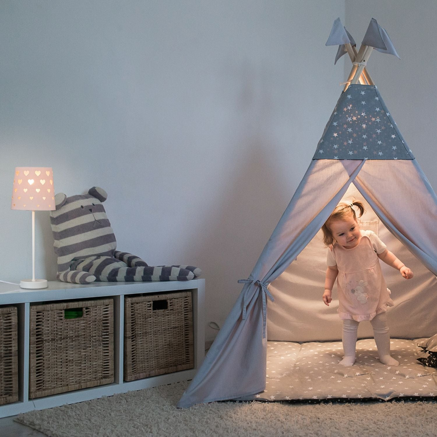 Una niña pequeña con vestido rosa está dentro de una tienda tipi iluminada.