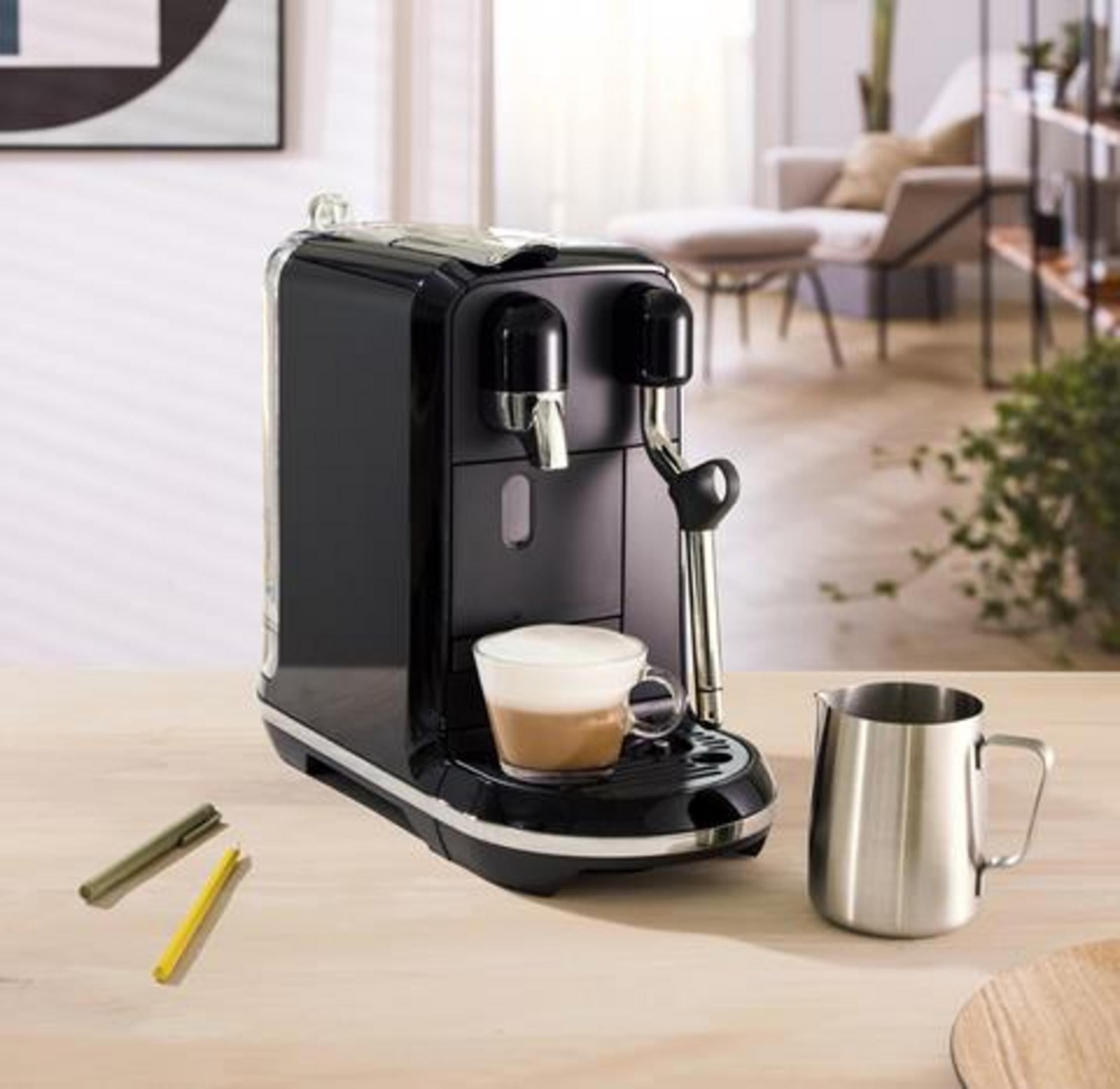 Eine schwarze Kaffeemaschine mit einer Tasse Kaffee, einem Milchkännchen und Stiften.