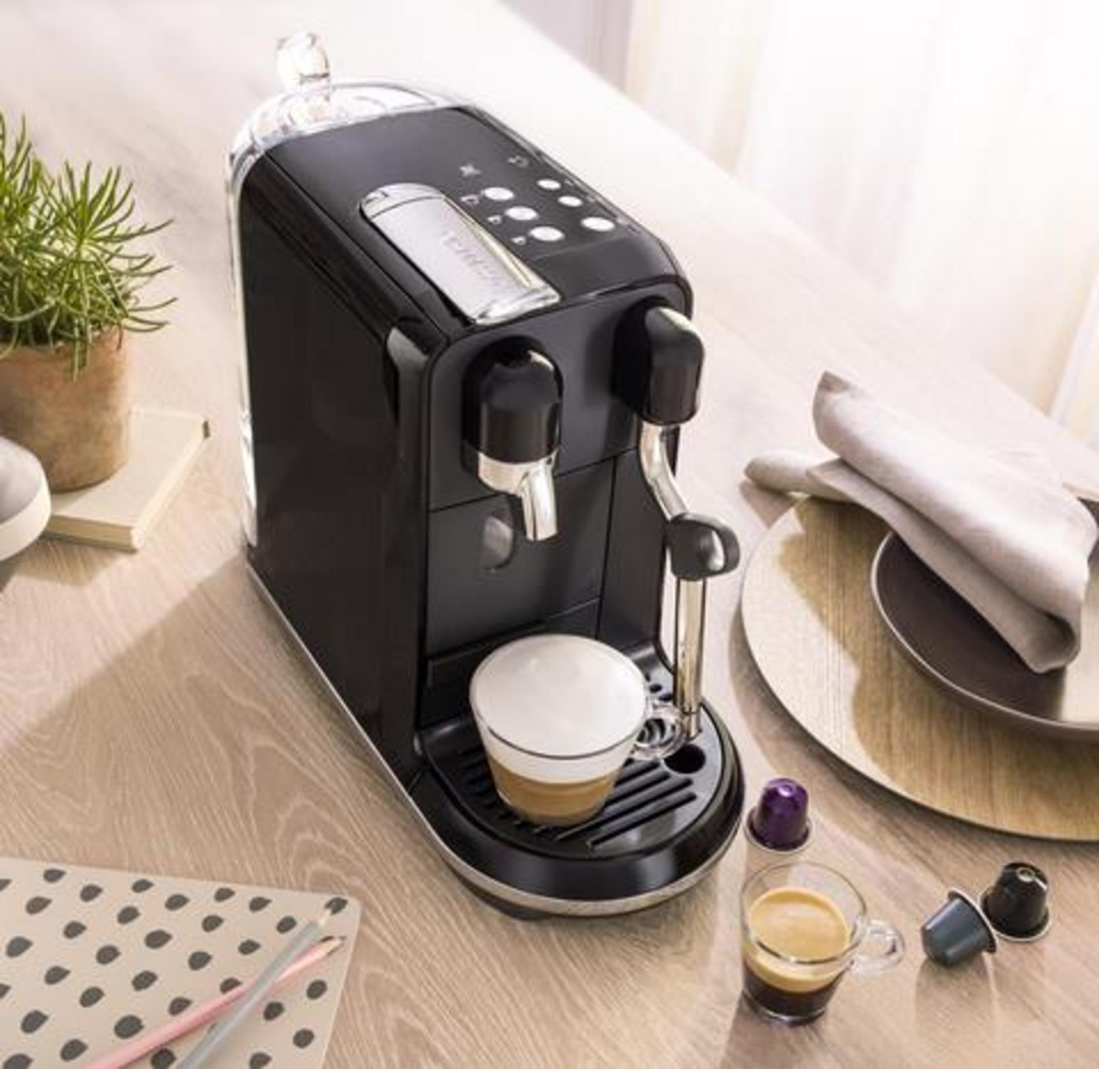 Schwarze Kaffeemaschine mit einer Tasse Kaffee und Kapseln auf einem Holztisch.