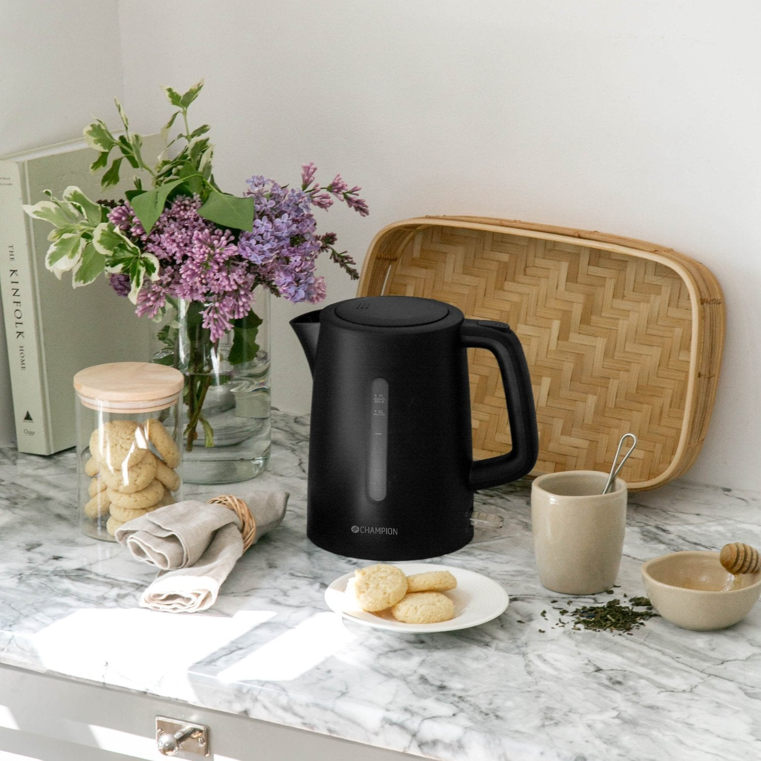 Black kettle with cookies, flowers, and tea on a marble countertop.
