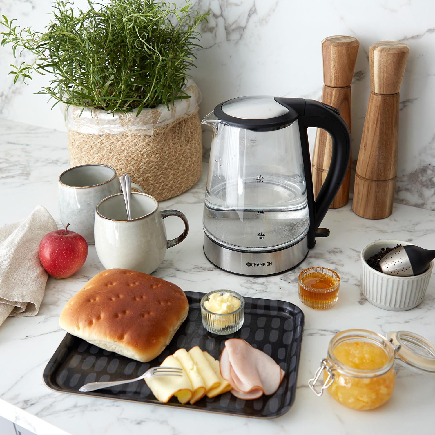 Ontbijtsetting met waterkoker, brood, kaas, ham, appel en jam.