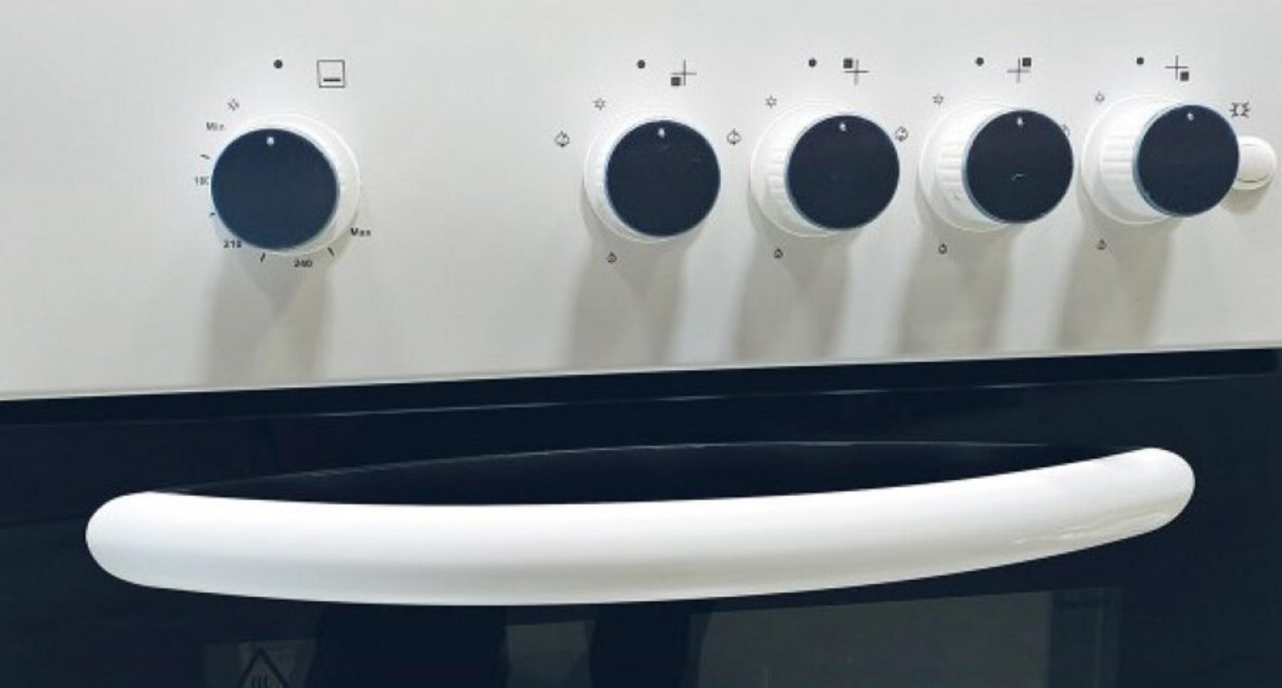 Zbliżenie czterech czarnych pokręteł na białym piekarniku z białym uchwytem.