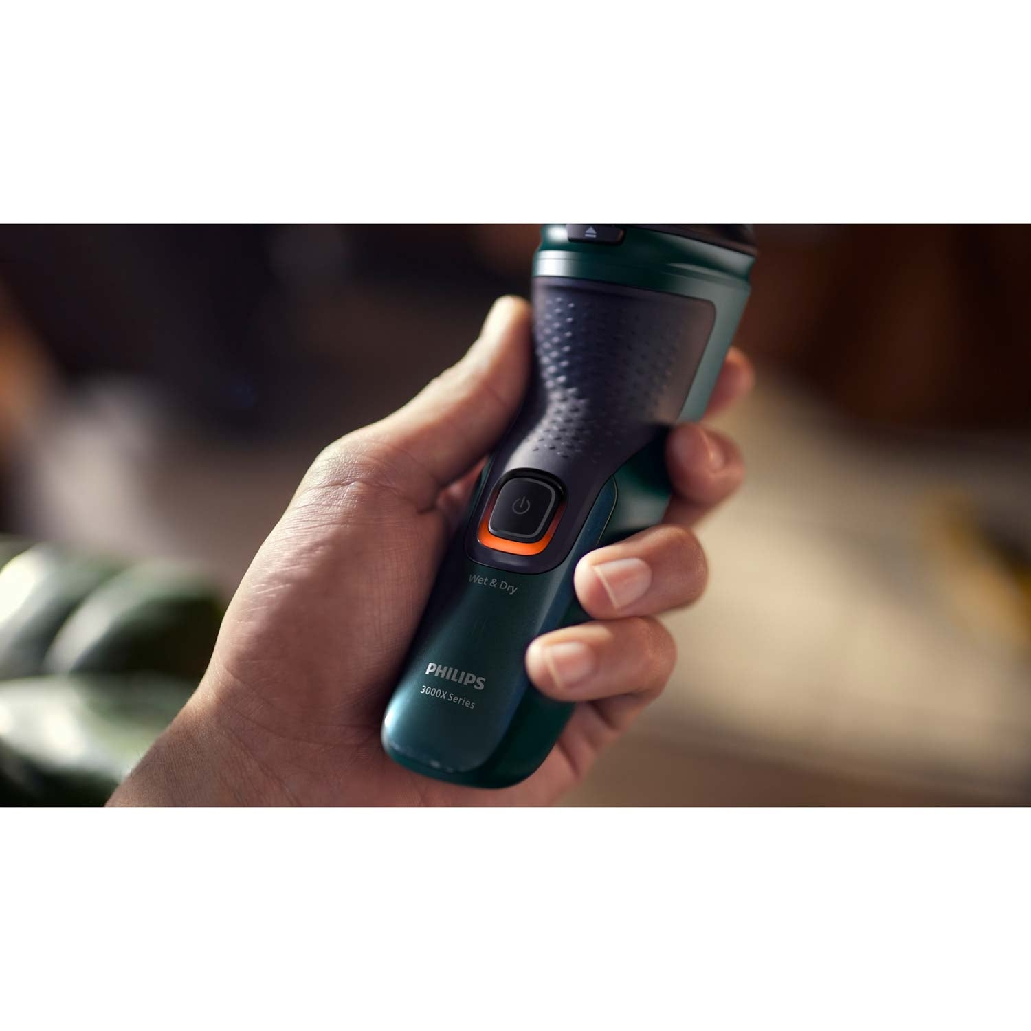 Una mano sostiene una afeitadora Philips verde oscuro con acento naranja.