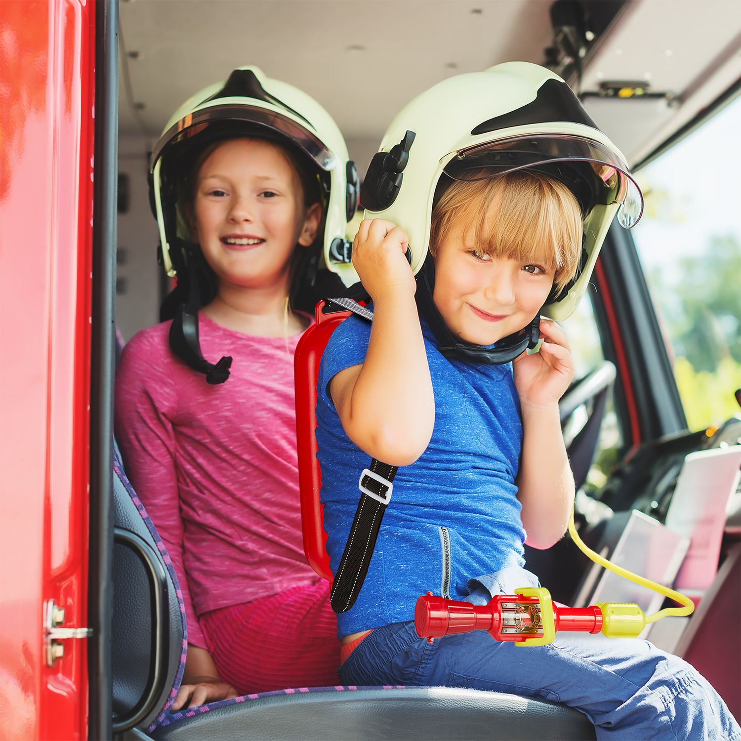 Dos niños con equipo de bombero sentados en un camión de bomberos rojo.