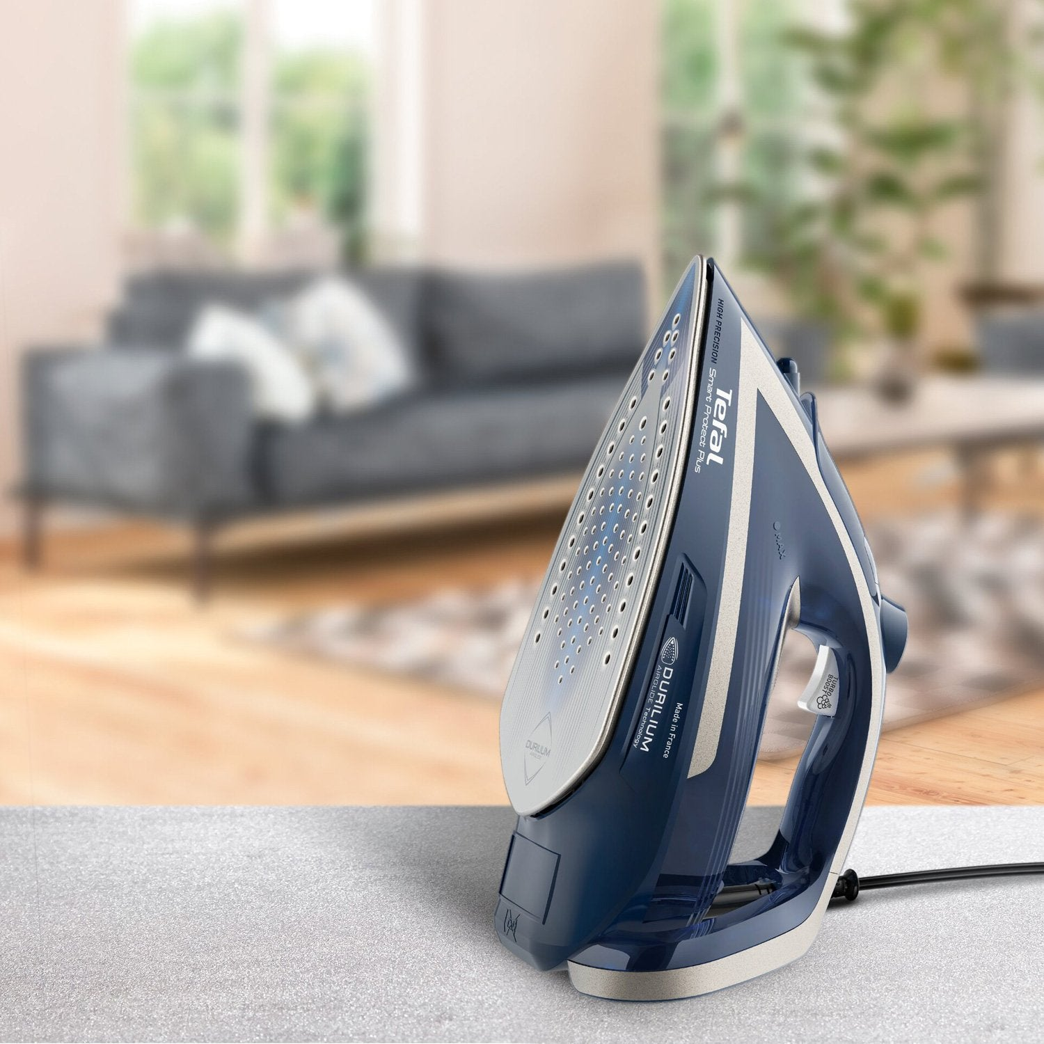 Una plancha de vapor Tefal azul descansa sobre una mesa frente a una sala de estar borrosa.