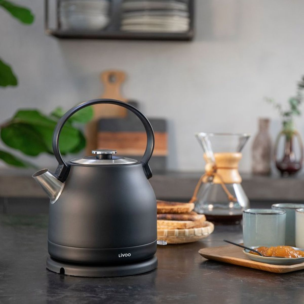 Bollitore nero con manico su piano di lavoro scuro, accanto a toast e caffè.