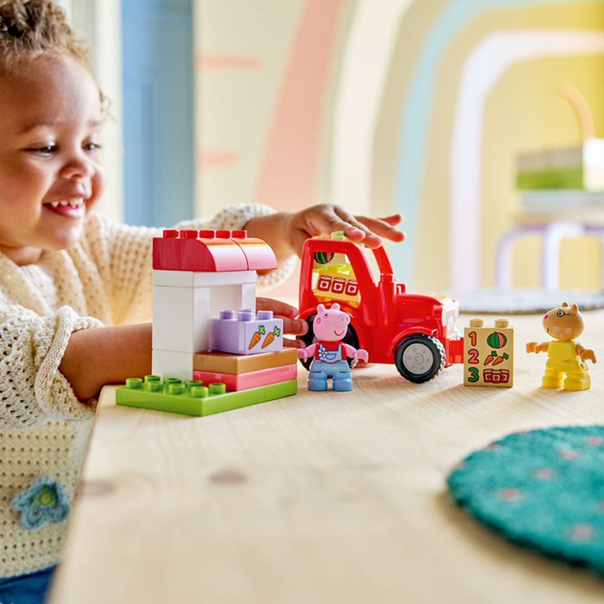 Dziewczynka bawi się figurkami Lego Duplo, czerwonym samochodem i straganem.