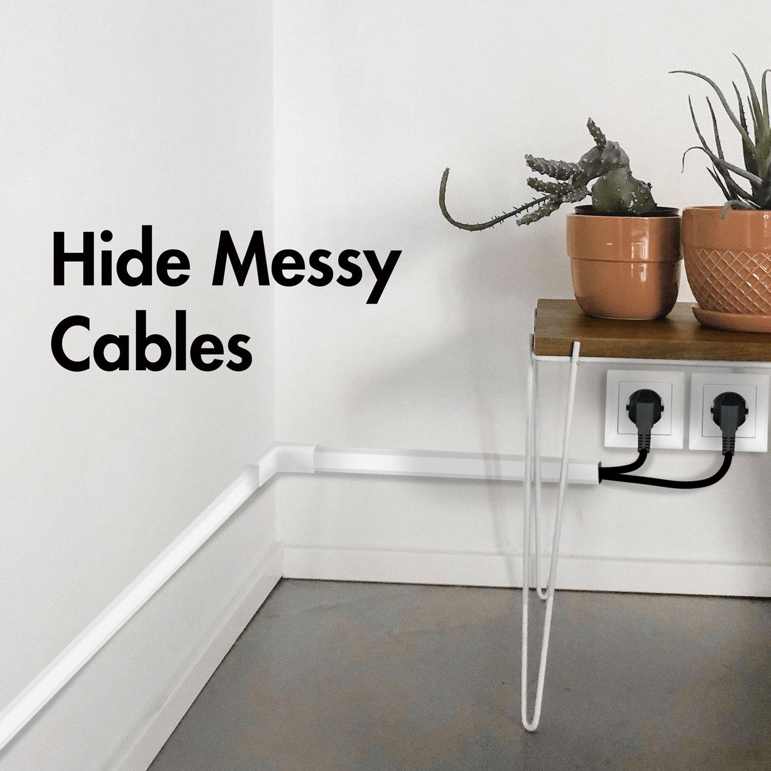 Canales blancos de gestión de cables ocultan cables en una esquina de pared. Dos enchufes se conectan a tomas.