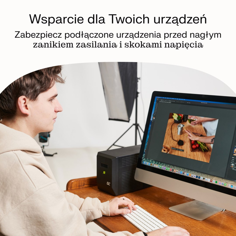 Mężczyzna siedzi przy biurku, pracuje na komputerze. Obok stoi zasilacz.