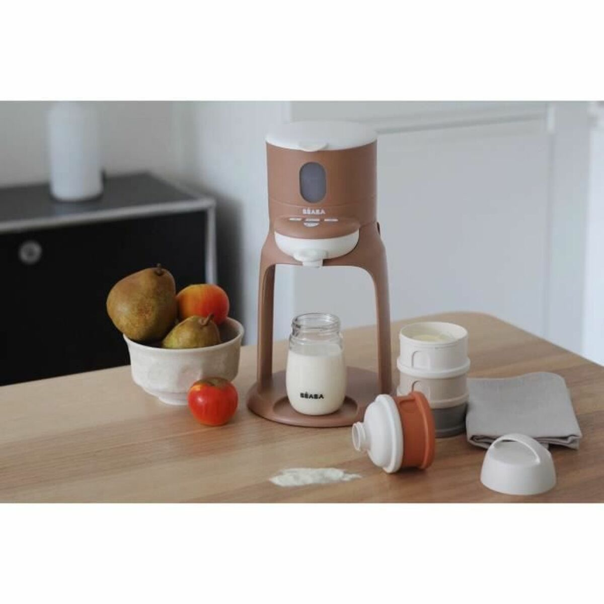 Ein brauner Babykostzubereiter mit Früchten, Milchflasche und Zubehör auf einem Holztisch.