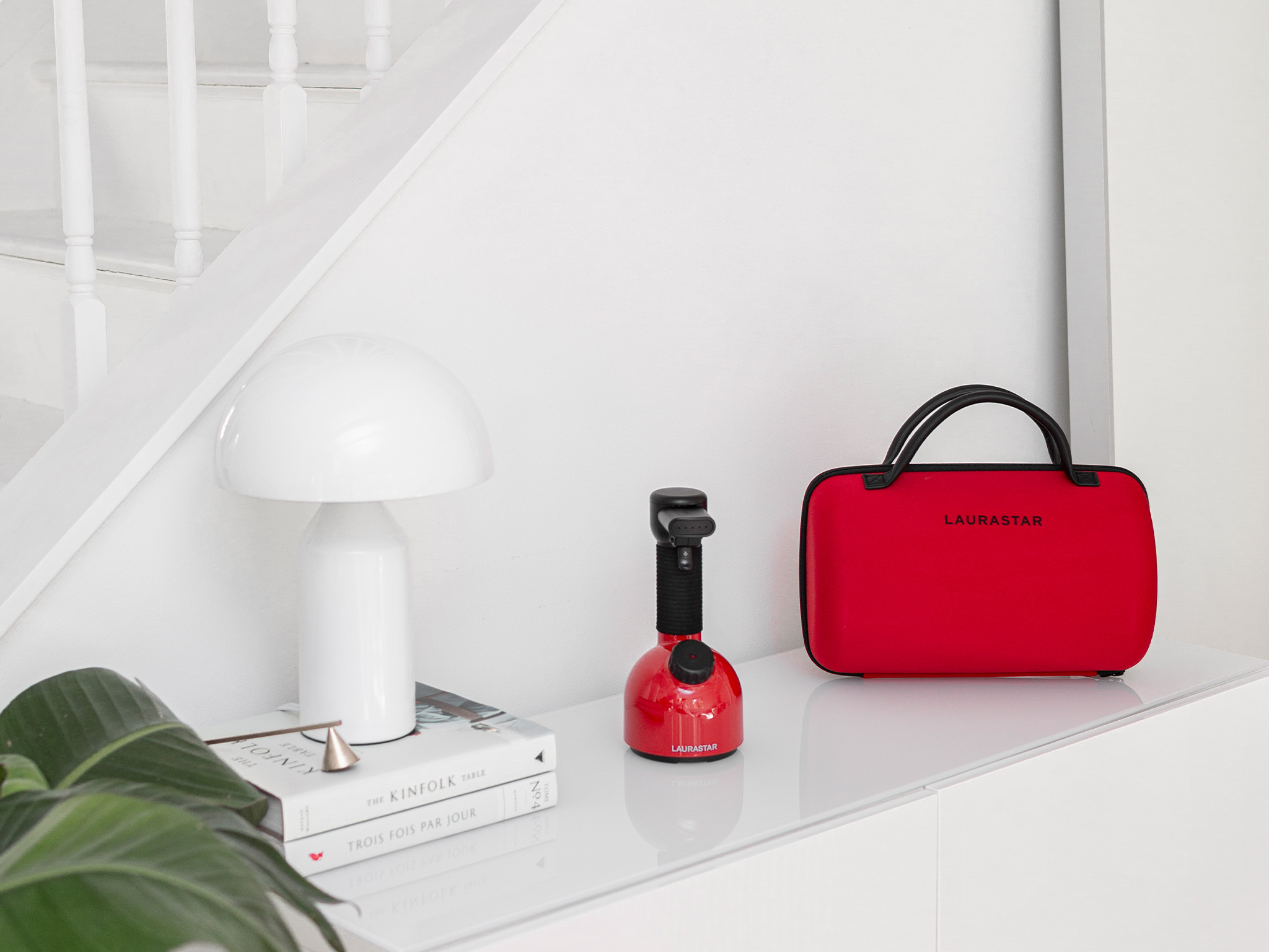 Ein weißer Tisch zeigt Bücher, eine weiße Lampe, einen roten Dampfer und eine rote LAURASTAR Tasche.
