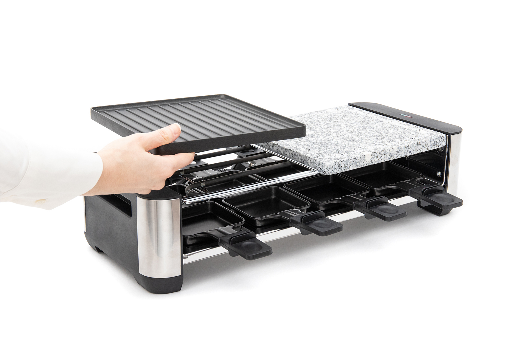 A hand places a grill plate onto a raclette grill with stone top and pans.