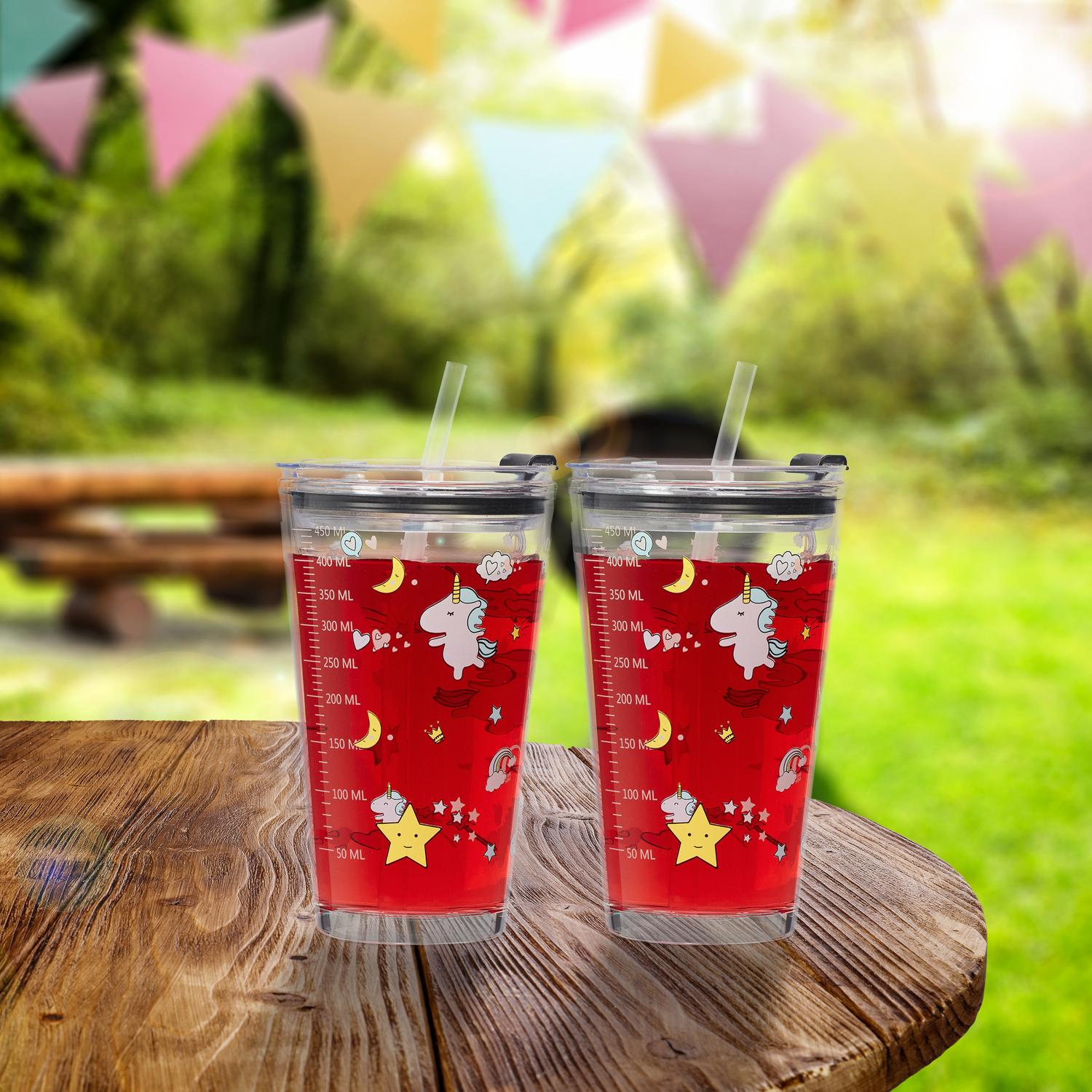 Dos vasos transparentes con líquido rojo y diseños de unicornio se sientan en una mesa de madera al aire libre.