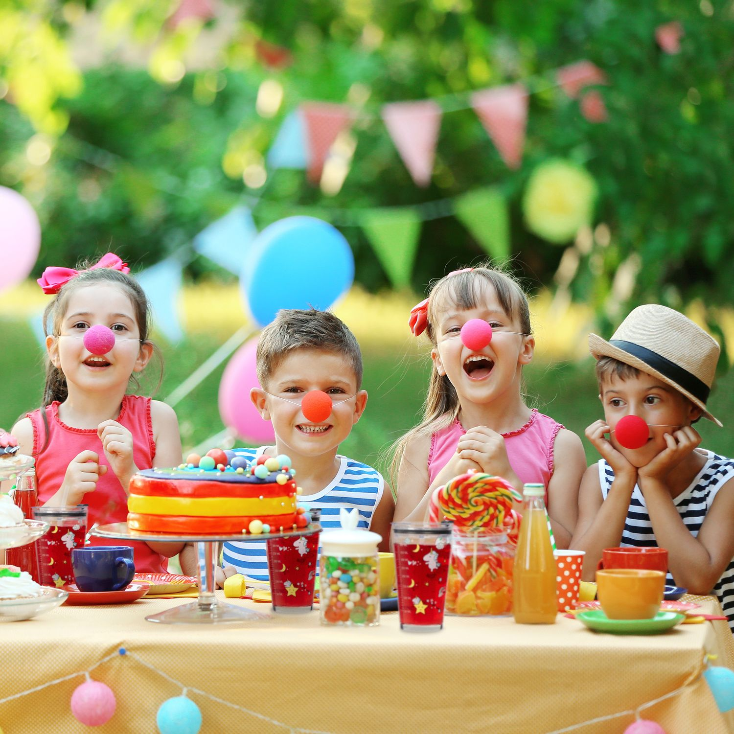 Cuatro niños con narices rojas sentados en una mesa en una fiesta al aire libre.