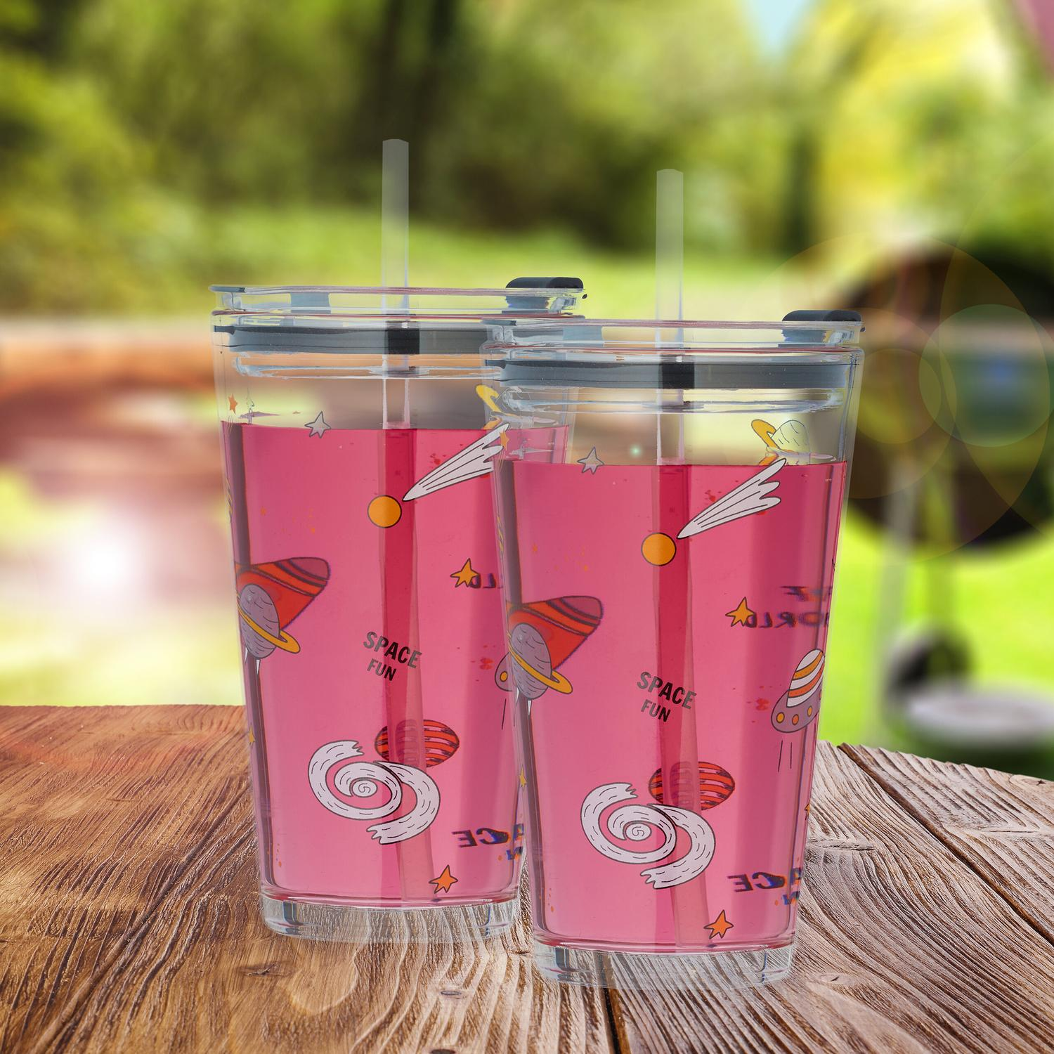 Dos vasos rosas temáticos del espacio con pajitas están sobre una mesa de madera.