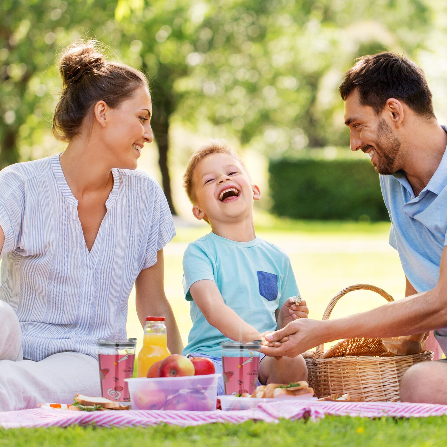 Una familia disfruta de un picnic al aire libre. El niño se ríe mientras los padres observan.