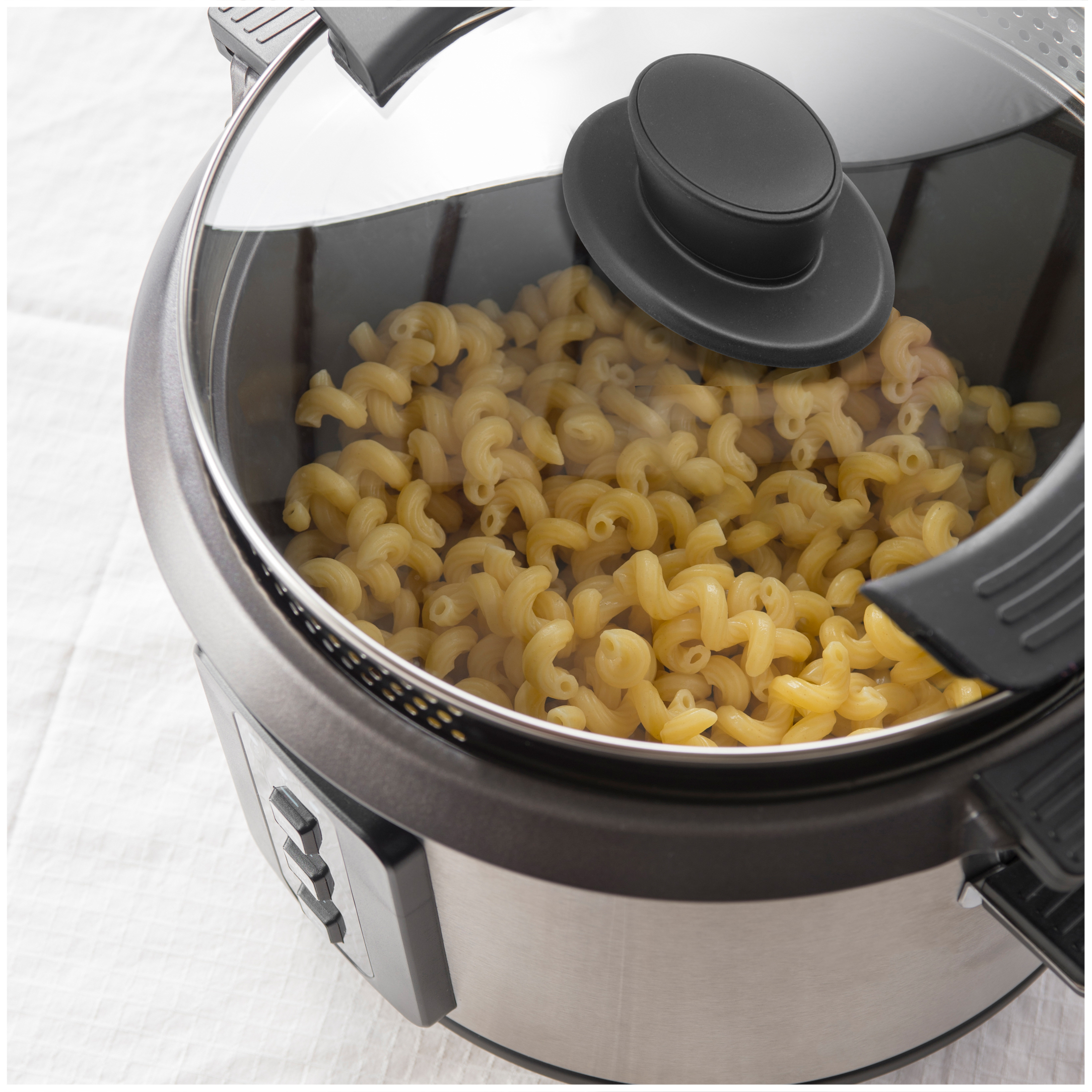 Steaming cavatappi pasta in a silver pot with a glass lid.