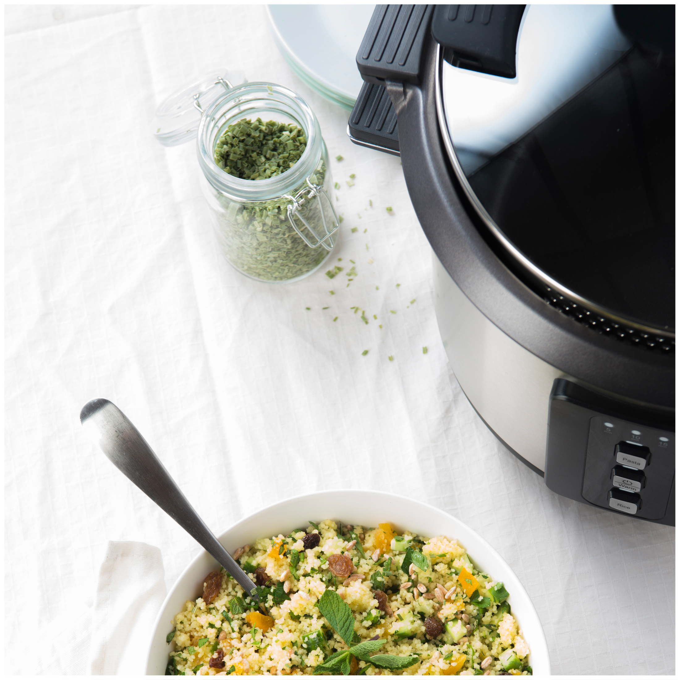 Couscous salad with raisins, apricots and mint next to a jar of herbs and a cooking appliance.