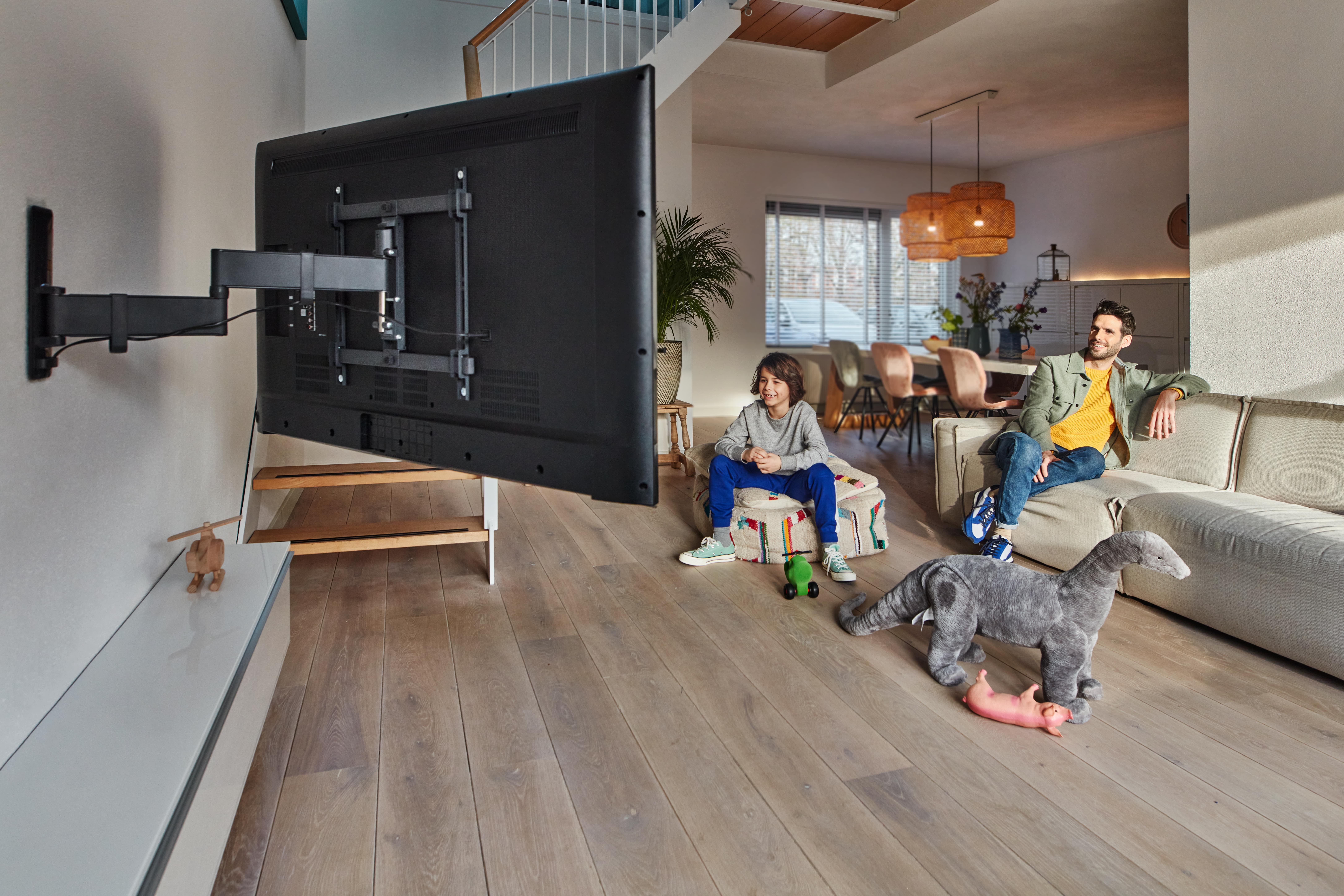 Chłopiec na pufie, mężczyzna na kanapie. Zabawka dinozaura leży na podłodze.