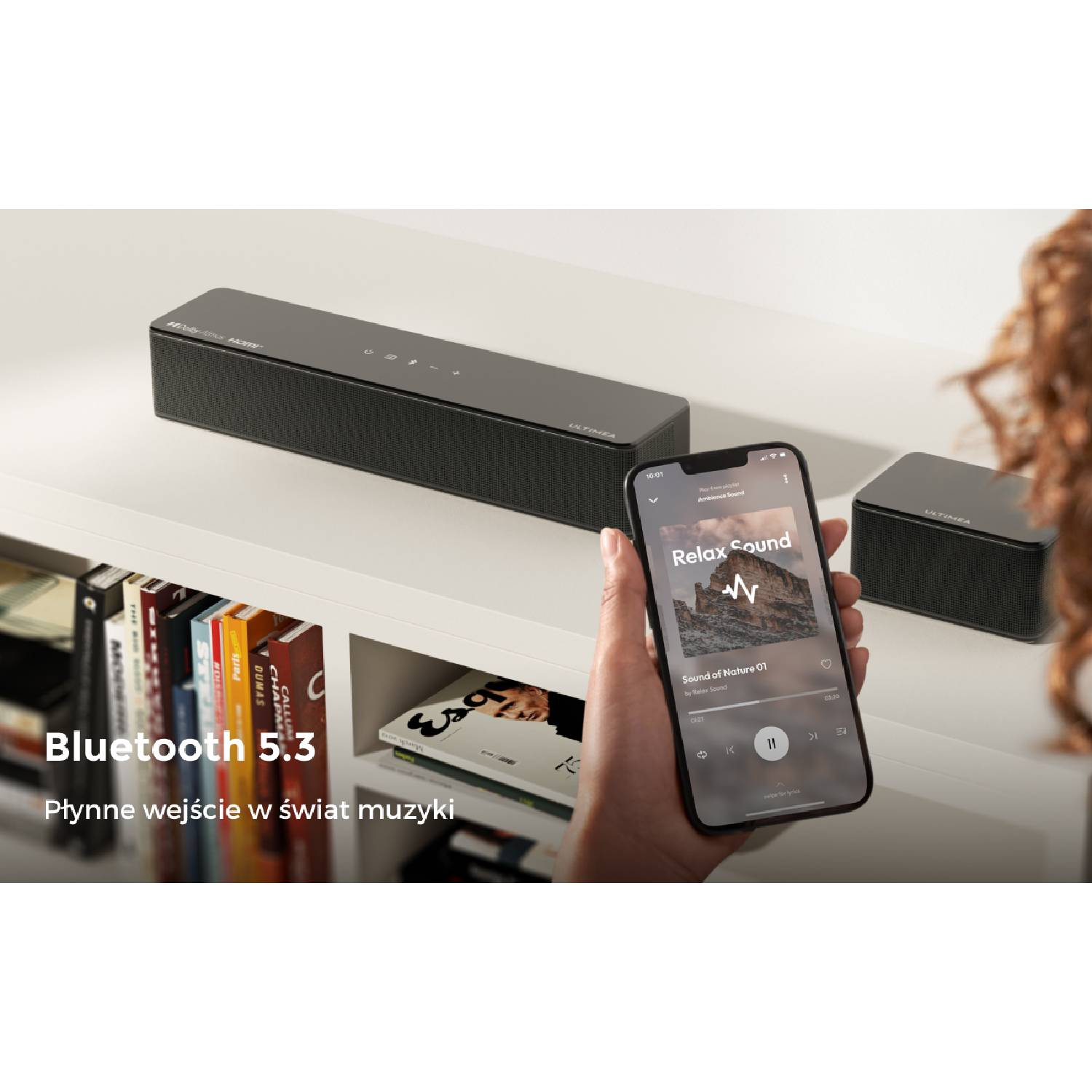 Smartfon steruje soundbarem z muzyką. Po lewej półka z książkami.