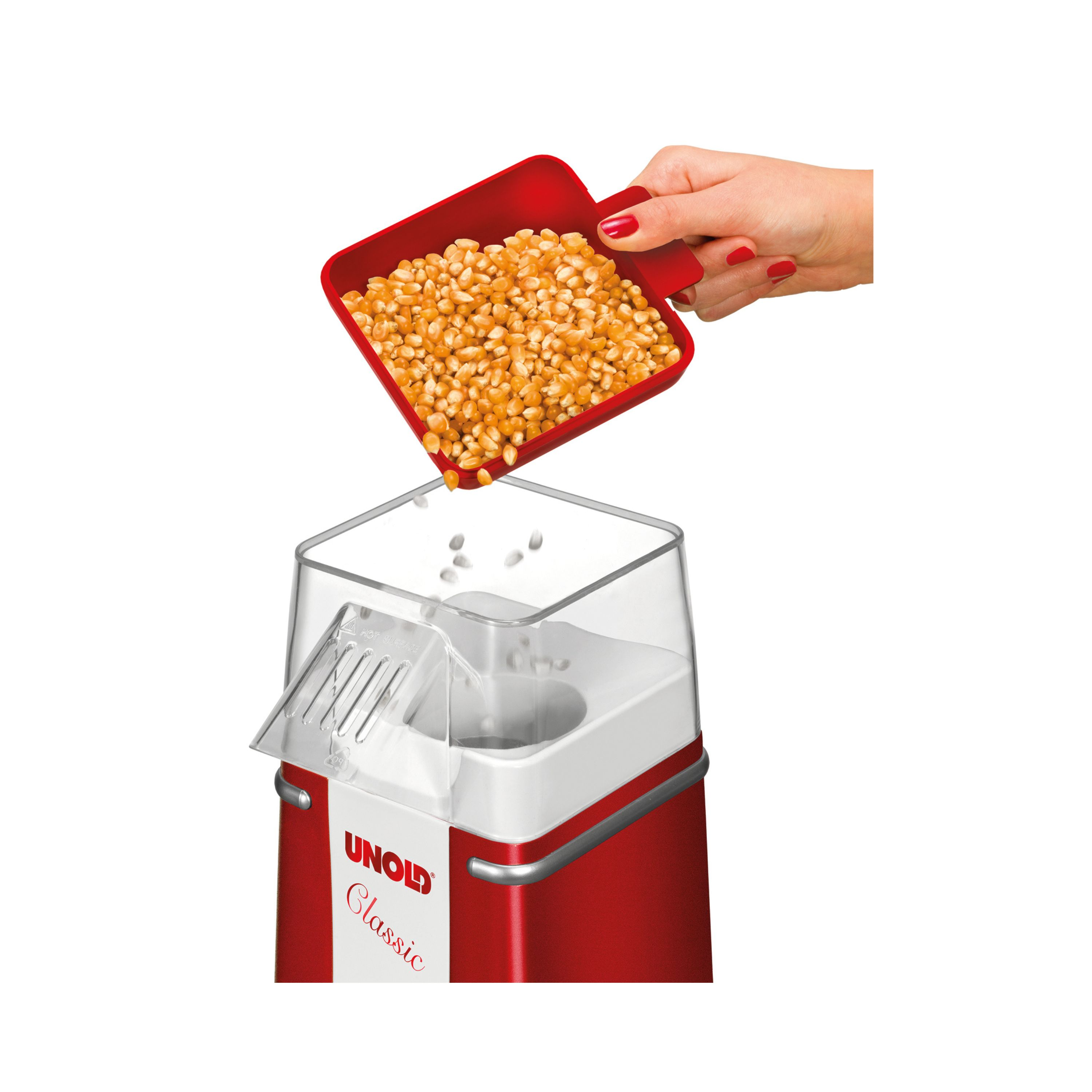 Eine Hand schüttet Maiskörner in einen roten Popcorn-Maker.