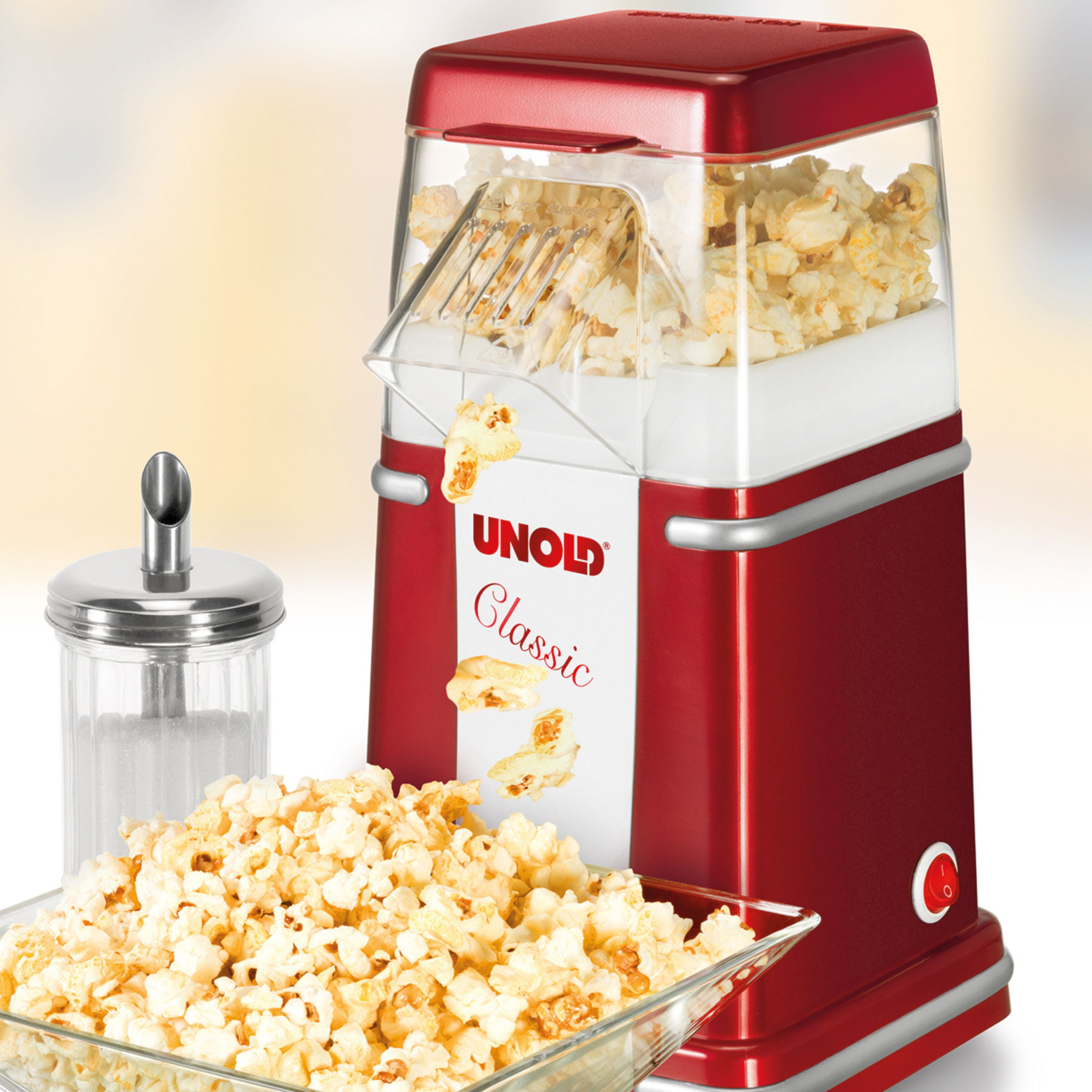 Ein roter Popcornautomat mit Popcorn in einer Glasschale und einem Zuckerspender.