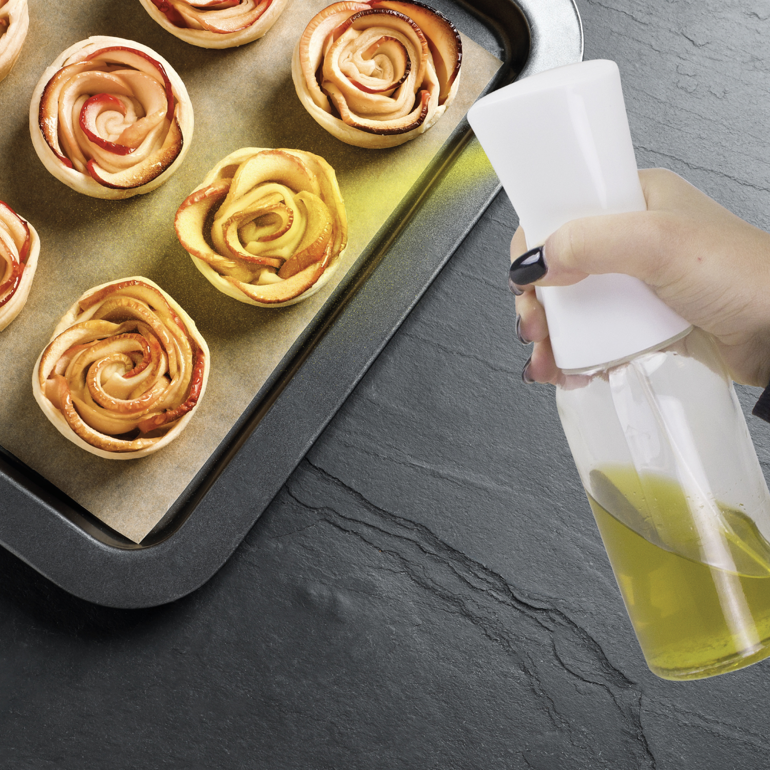 Mano spruzza olio su rose di mele al forno su una teglia.