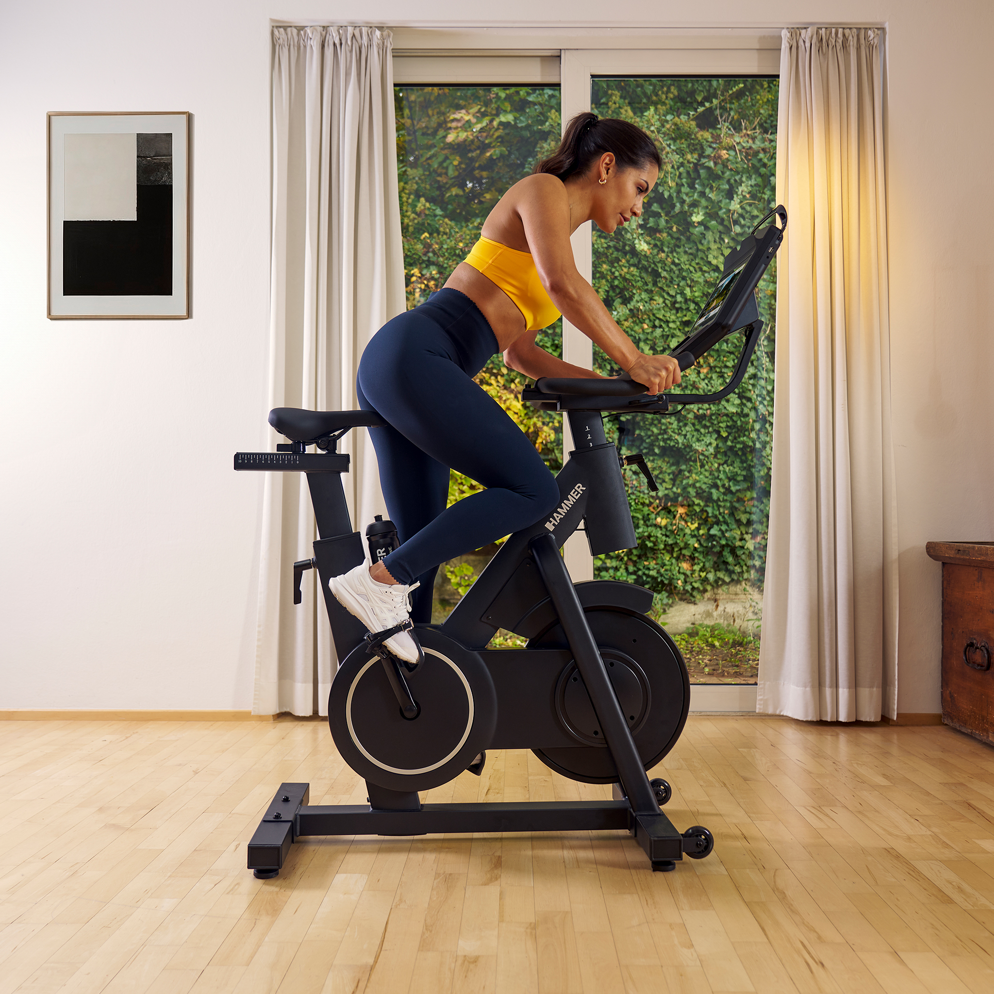 Eine Frau auf einem schwarzen Heimtrainer in einem hellen Raum mit Holzboden.