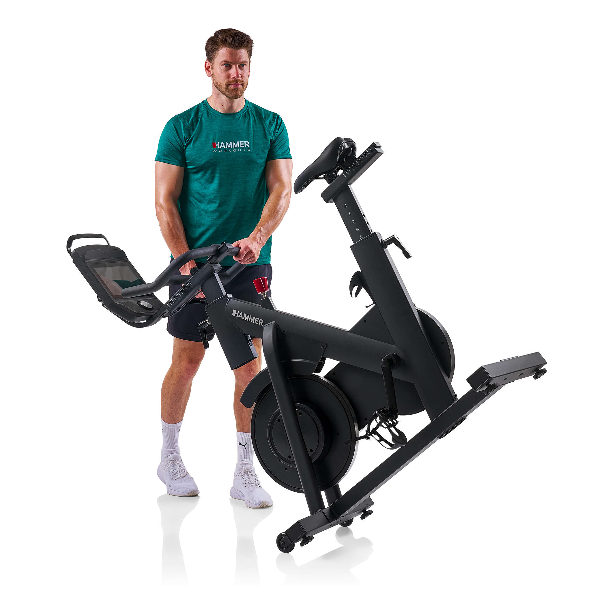 Ein Mann in einem grünen Trikot steht neben einem schwarzen Heimtrainer.