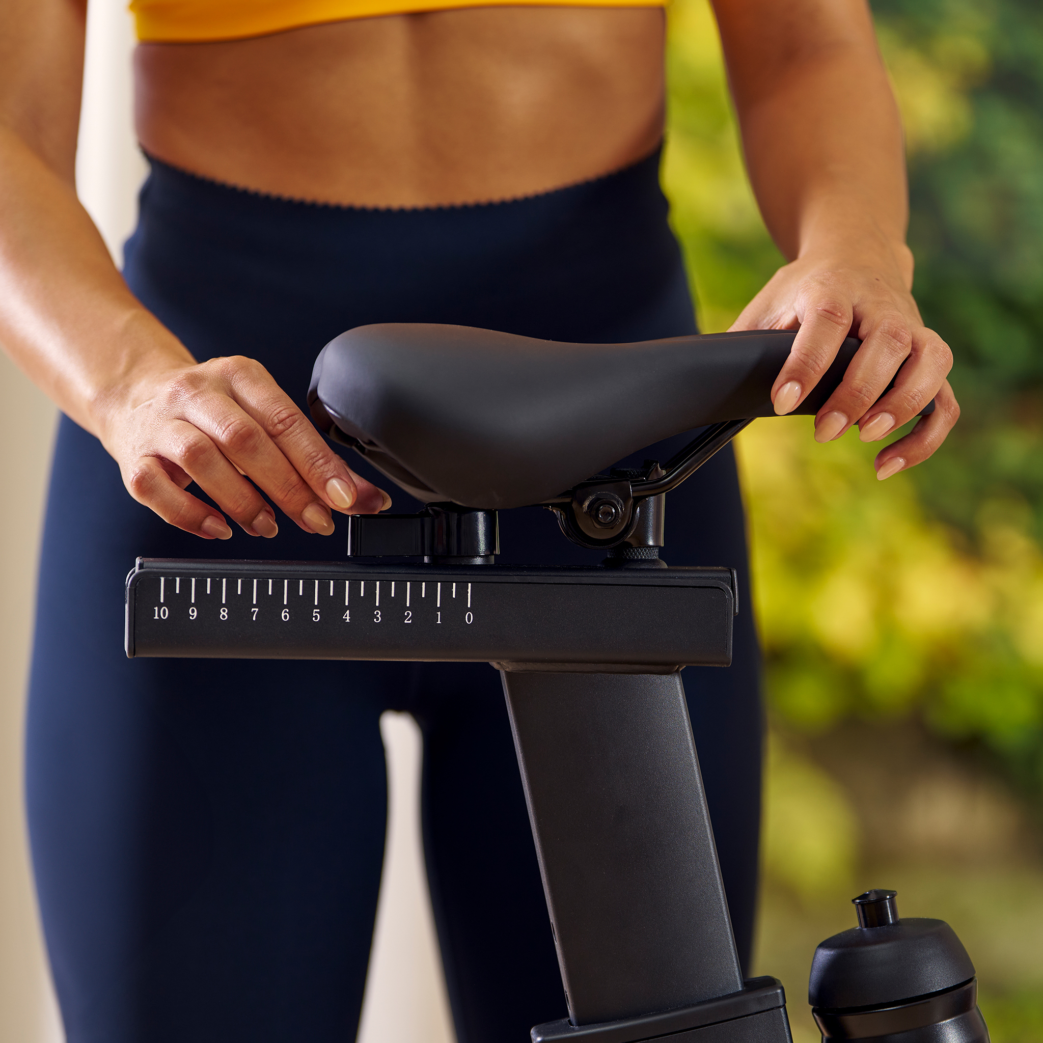 Frau stellt Sattel eines Heimtrainers ein. Sie trägt Sportkleidung.