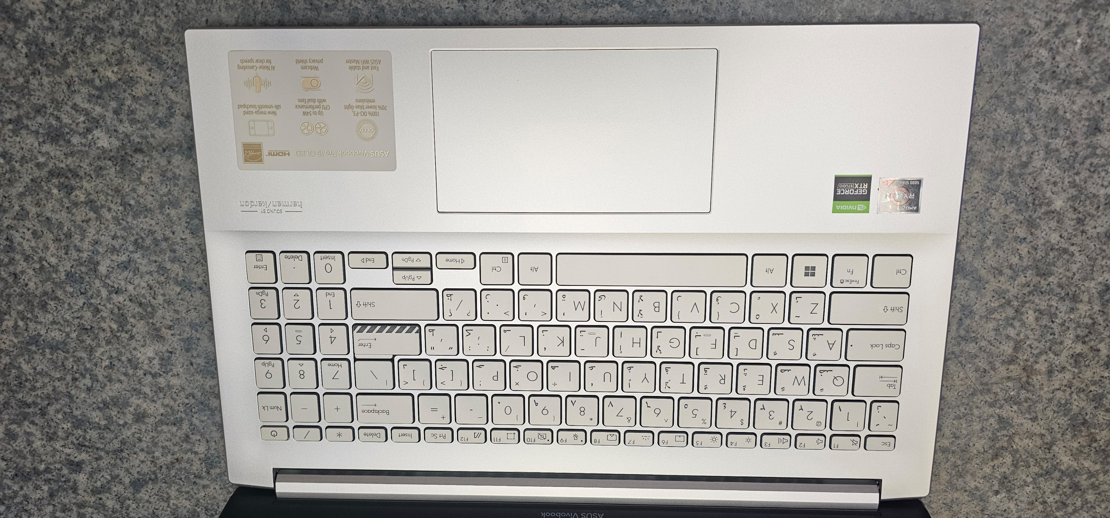 Srebrny laptop z klawiaturą, touchpadem i naklejkami. Widok z bliska.