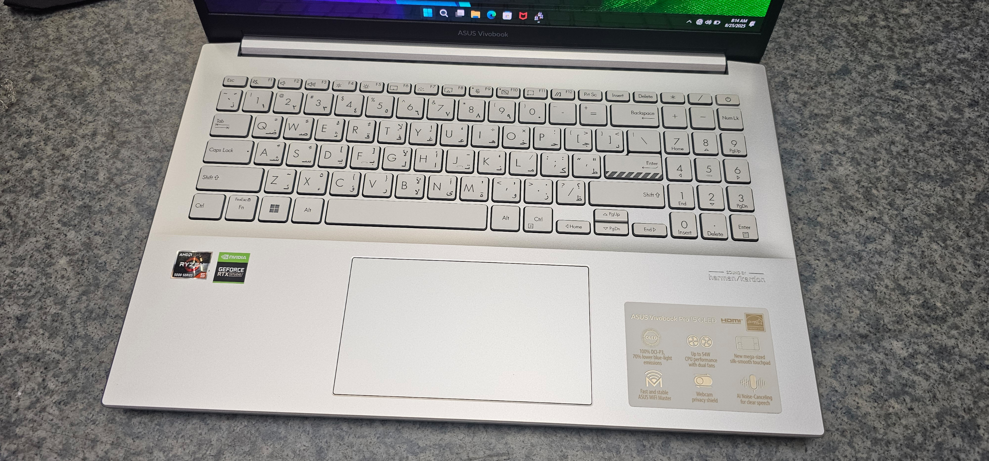 Srebrny laptop ASUS Vivobook pokazujący klawiaturę, touchpad i naklejki.