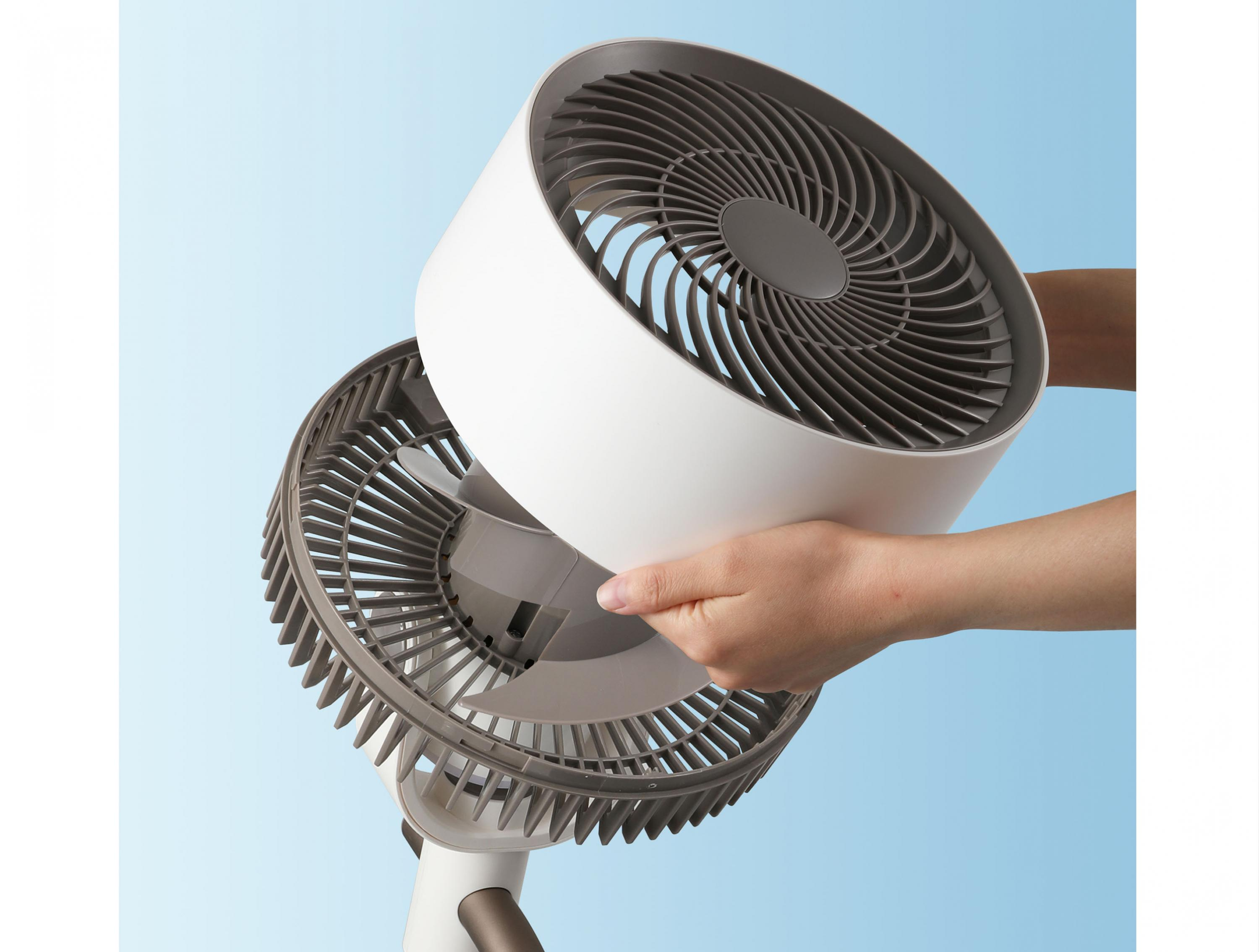 Una mano sujeta la parte superior de un ventilador blanco con rejilla gris.
