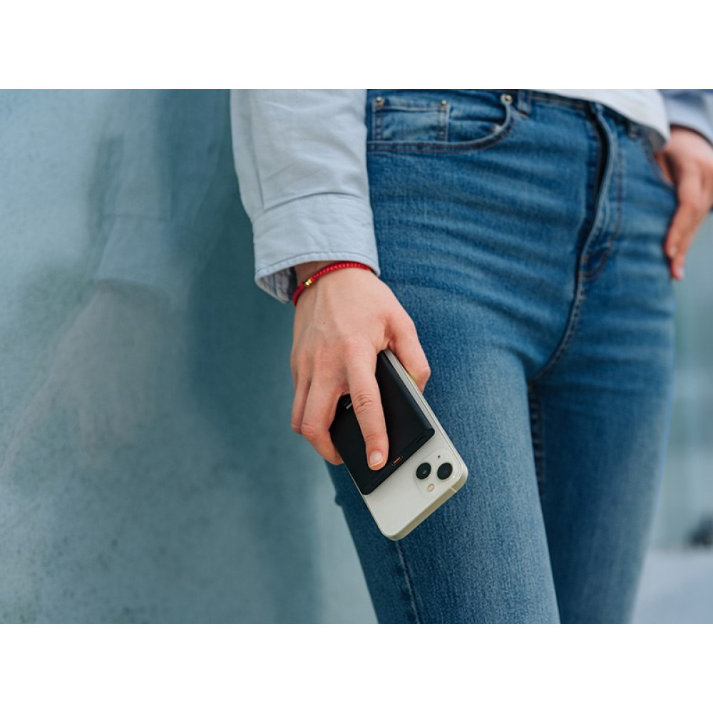 Osoba w dżinsach trzyma jasny smartfon z czarnym akcesorium.