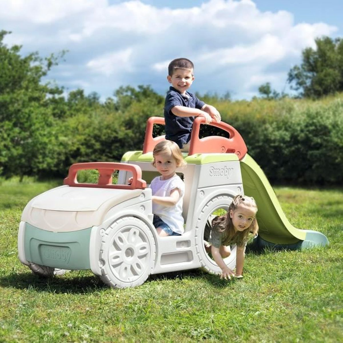 Tre bambini giocano su un'auto giocattolo con scivolo in un giardino.