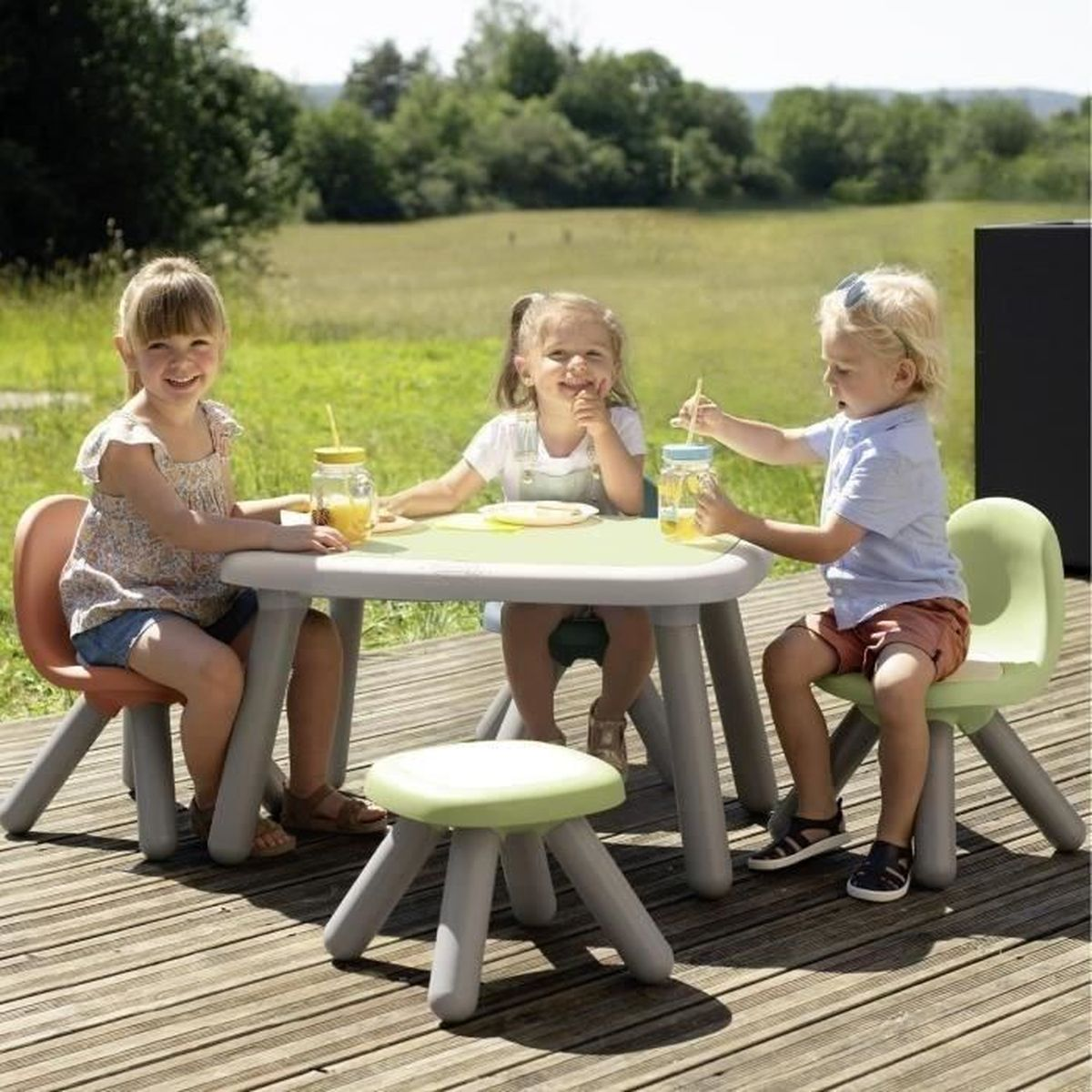 Tre bambini siedono a un tavolo all'aperto bevendo succo. Sono in estate.
