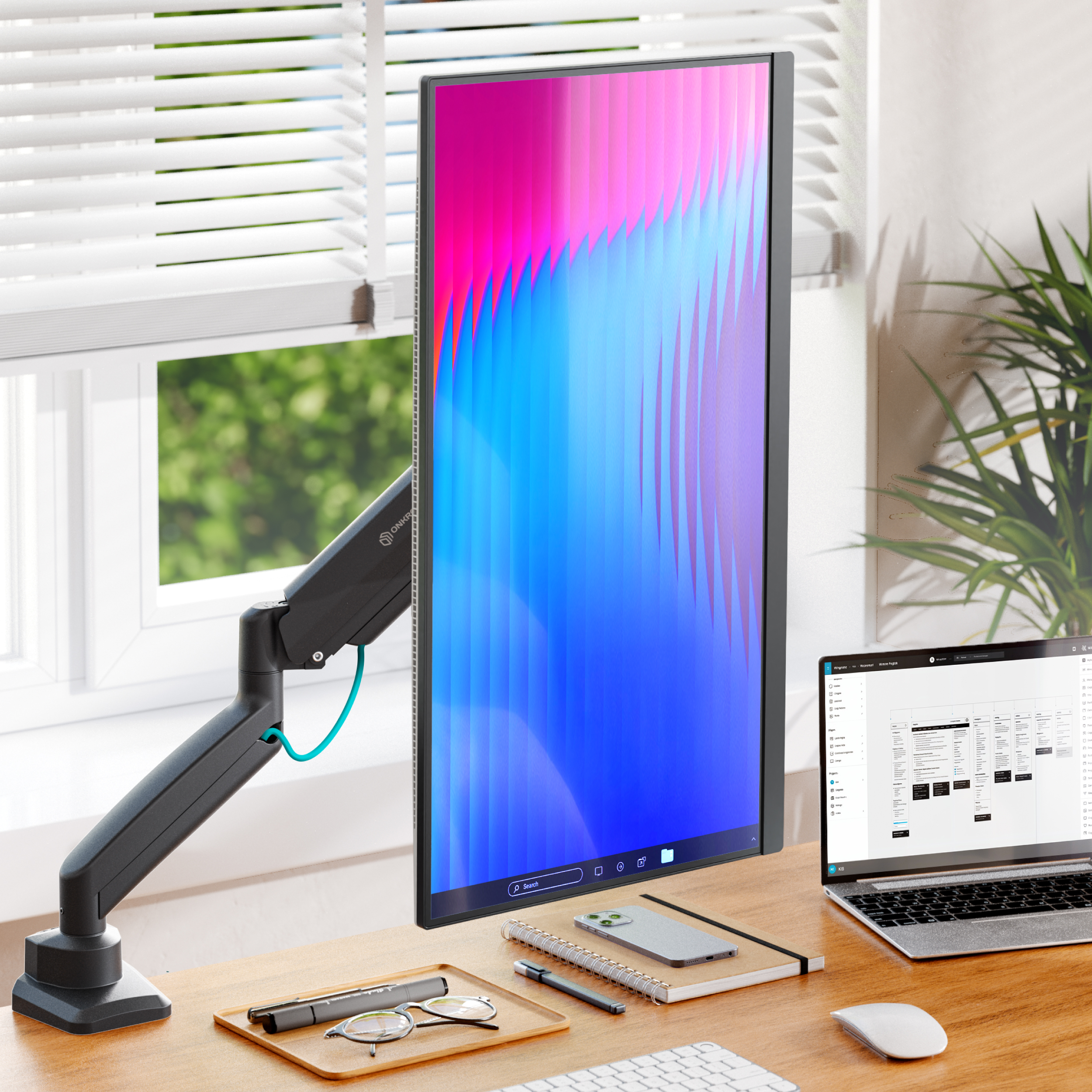 Biurko z pionowym monitorem, laptopem, telefonem i notatnikiem.