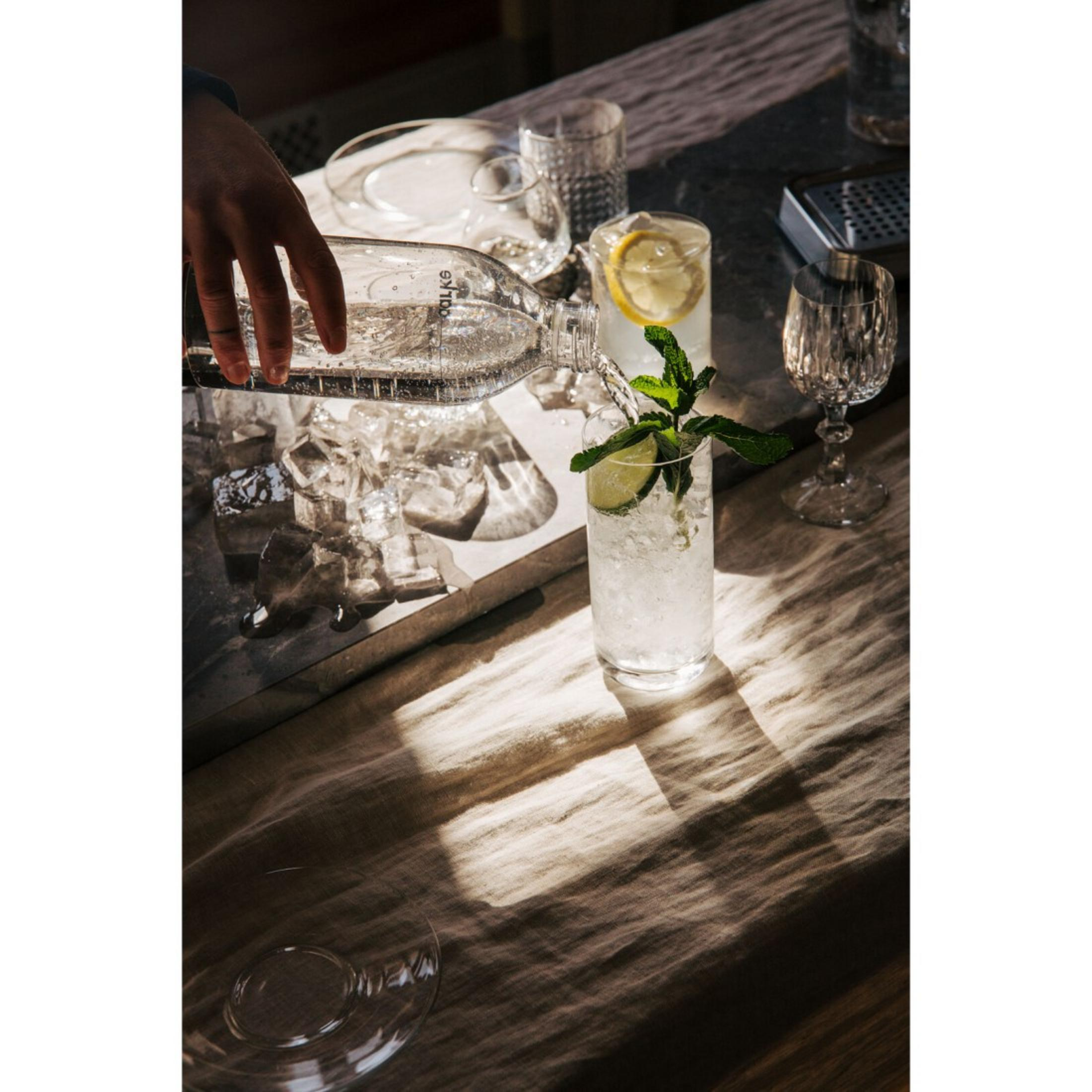 Wasser wird aus einer Flasche in ein Glas mit Eis, Minze und Limette gegossen.
