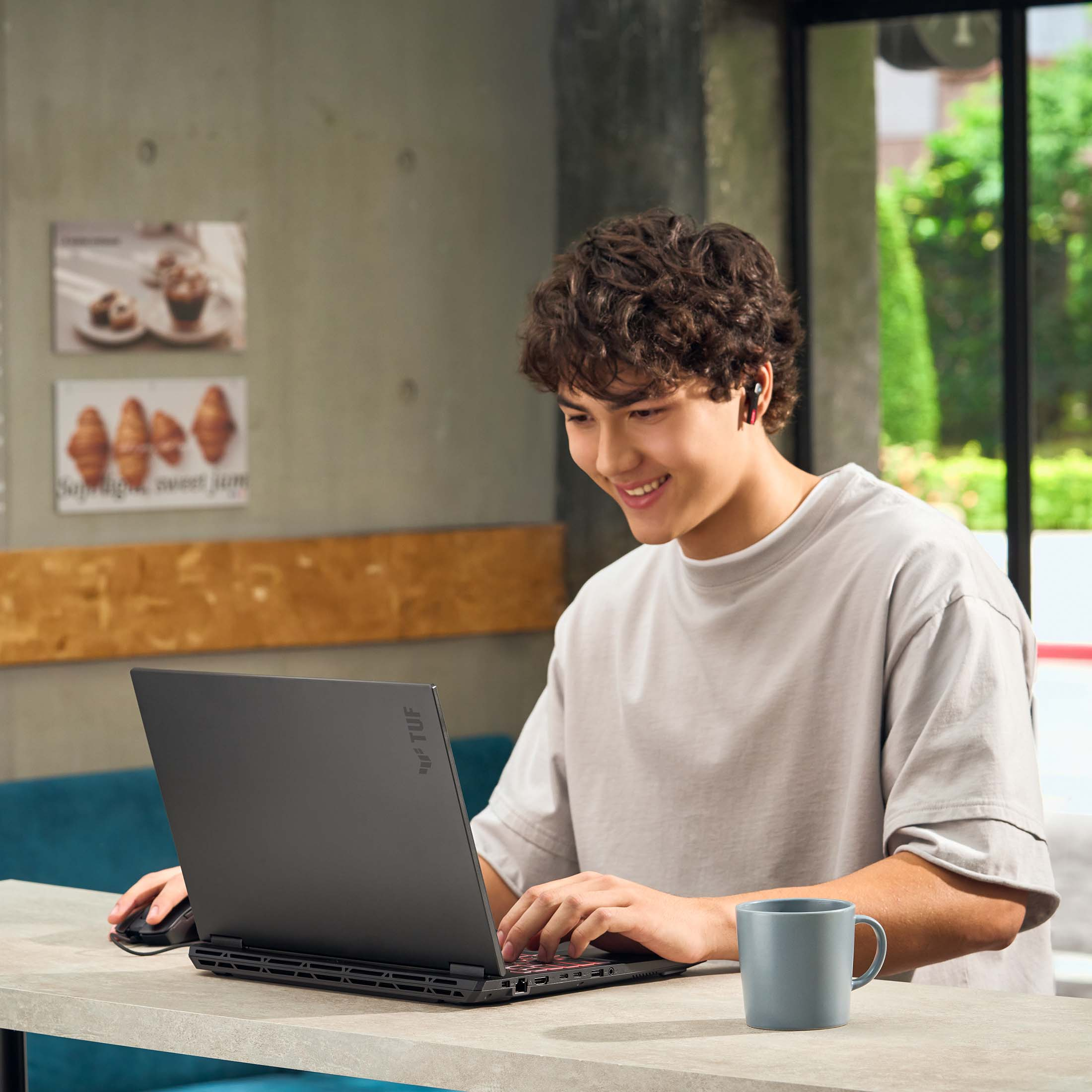 Ein junger Mann mit Locken sitzt an einem Tisch und benutzt einen Laptop. Er trägt Kopfhörer.