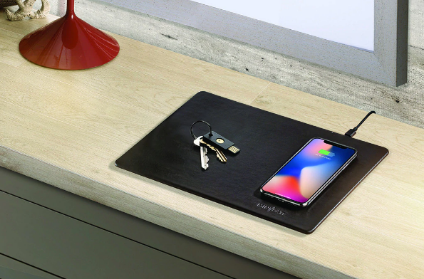 Un smartphone se carga en una alfombrilla de carga negra, con un llavero al lado.