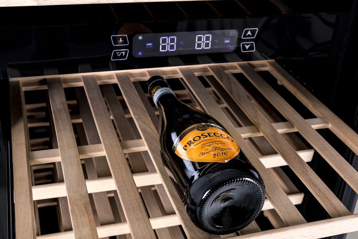 A bottle of Prosecco rests on wooden shelves inside a cooler with a digital display.