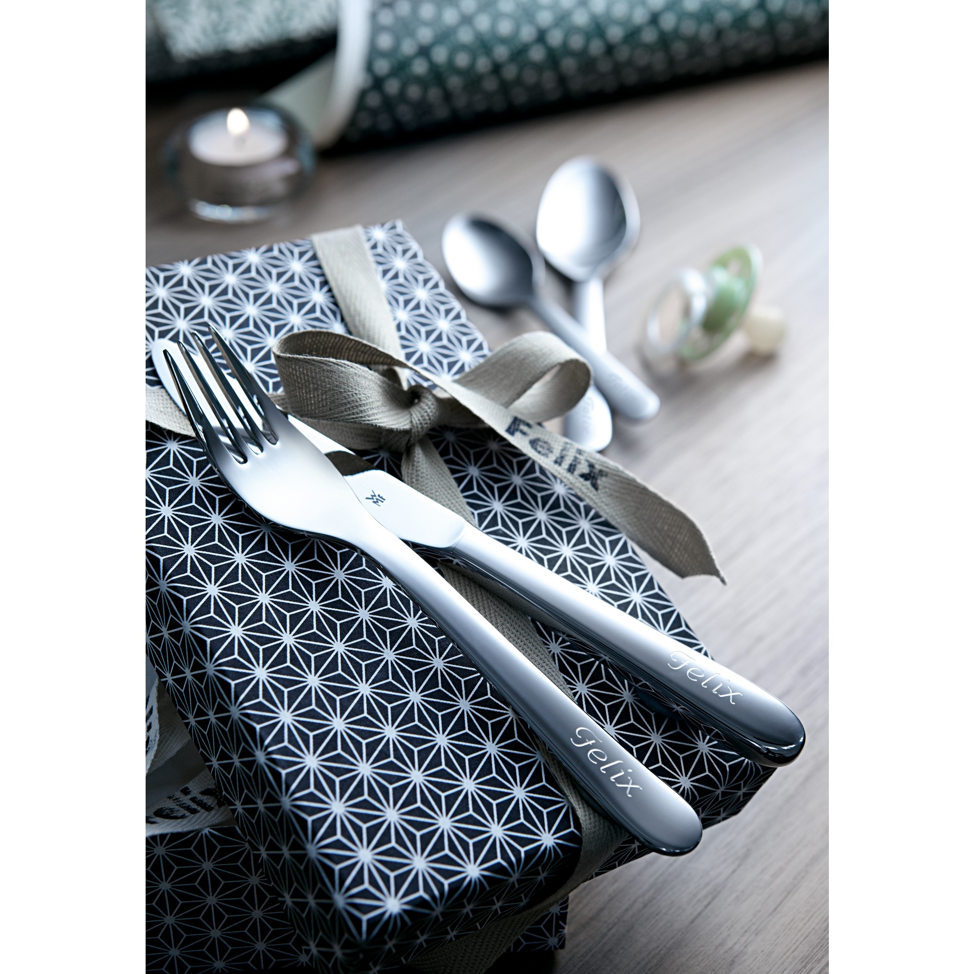 Ein Besteckset mit dem Namen "Felix" liegt auf einer Geschenkbox mit Muster.
