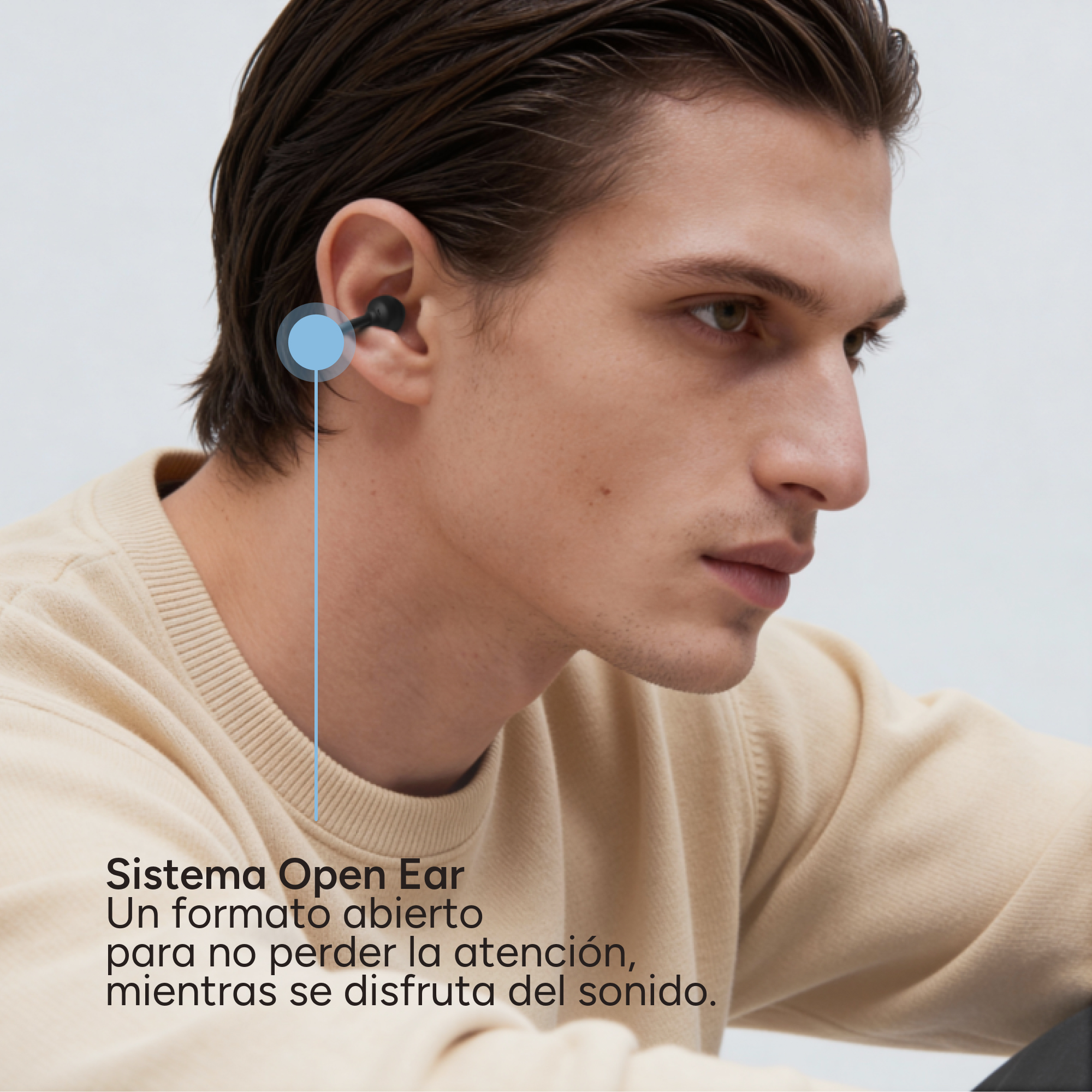 Hombre con un audífono en la oreja. Suéter beige. Fondo gris.