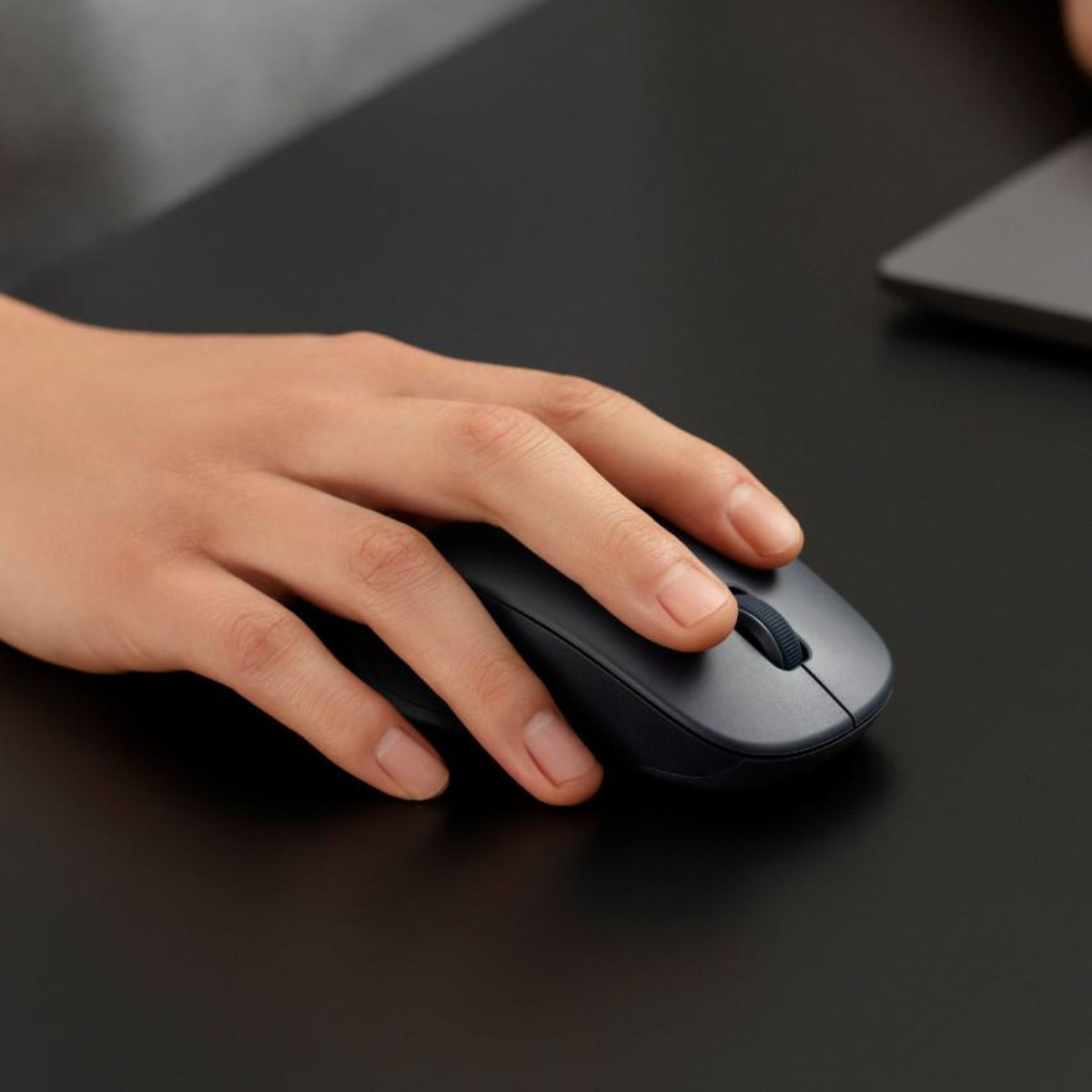 Una mano aziona un mouse scuro su una scrivania nera.