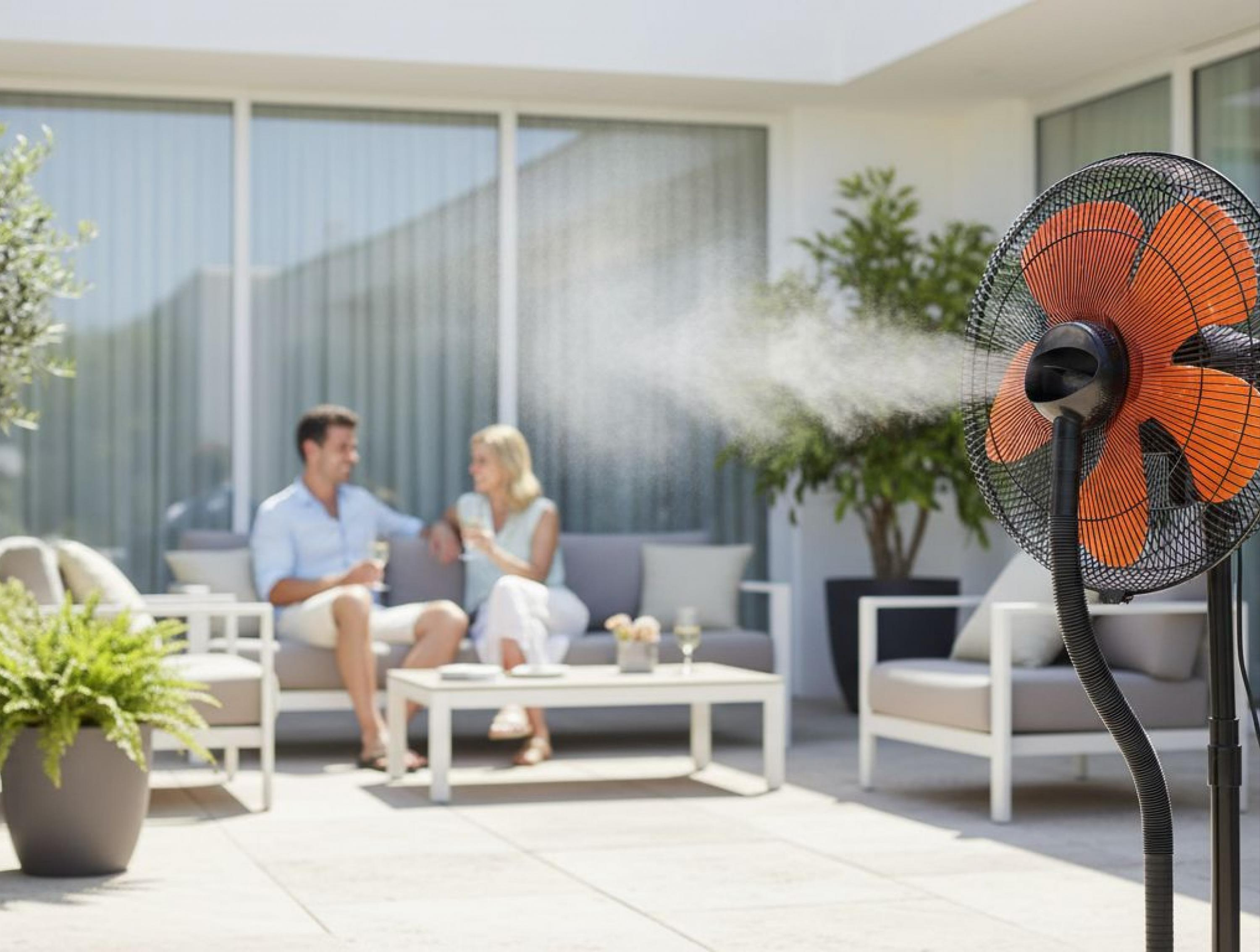 Ein Nebelventilator kühlt ein Paar auf einer Terrasse mit einem Sofa und einem Tisch.